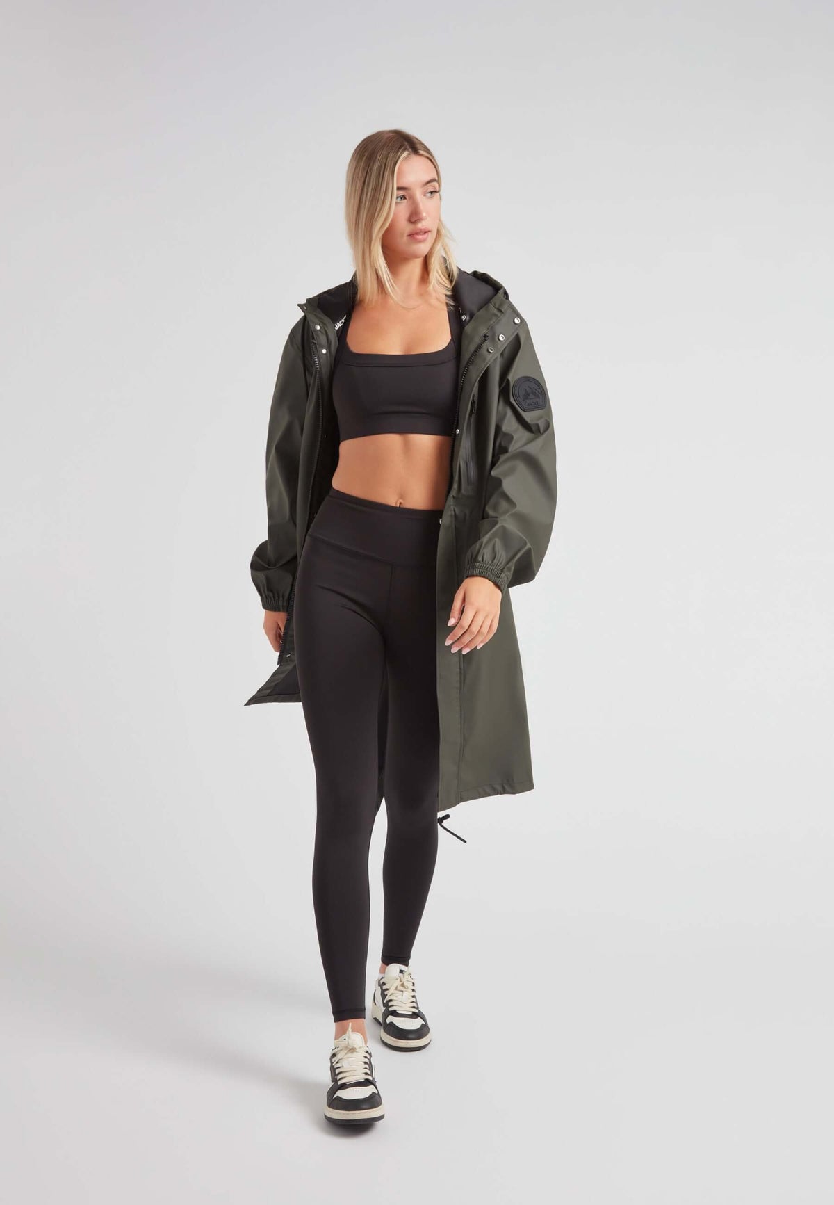 Model wearing ELEMENTS unisex raincoat in khaki over black activewear, showcasing stylish outdoor wear.