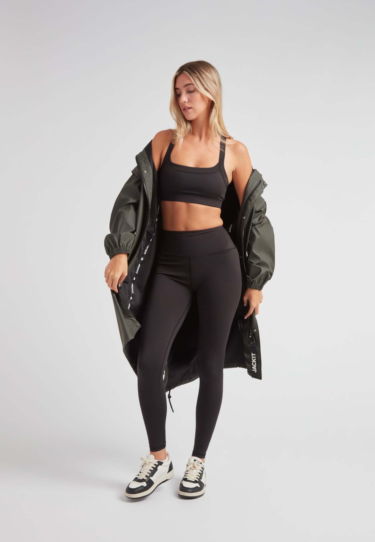 Model wearing ELEMENTS unisex raincoat in khaki with black leggings and crop top.
