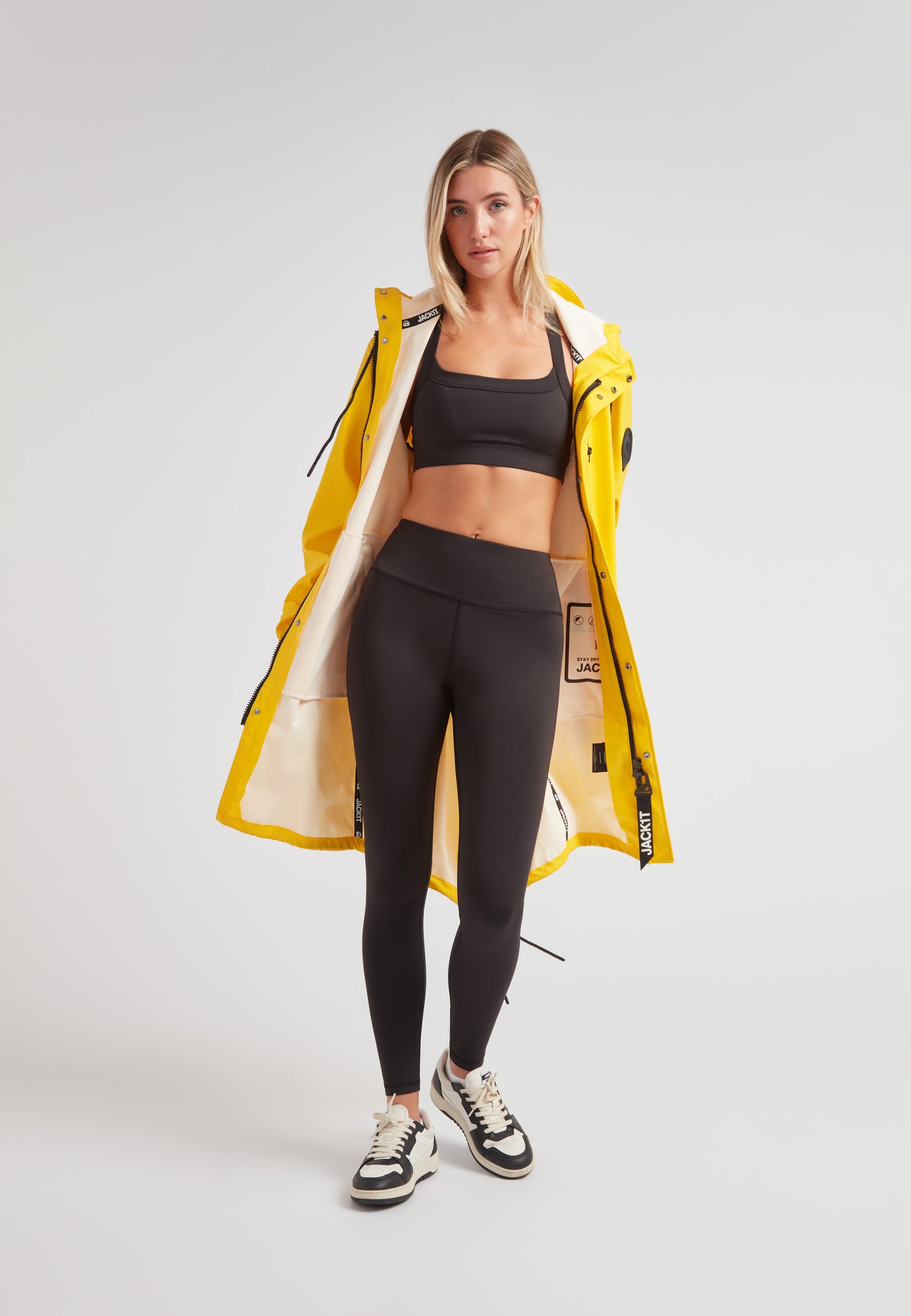 Model wearing a yellow ELEMENTS longline raincoat 2.0 with black leggings and a sports bra.