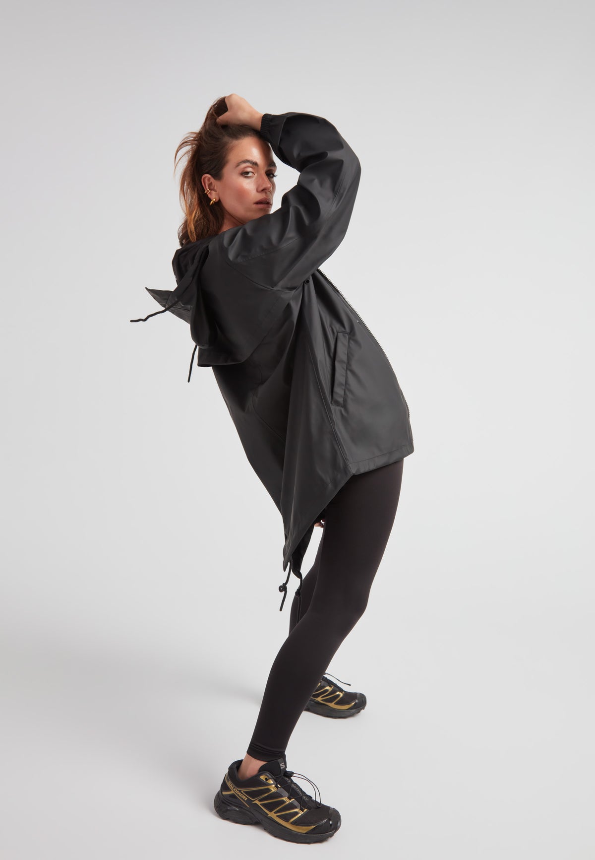 Model wearing ELEMENTS Raincoat 2.0 Black with leggings and athletic shoes, showcasing lightweight weather protection.