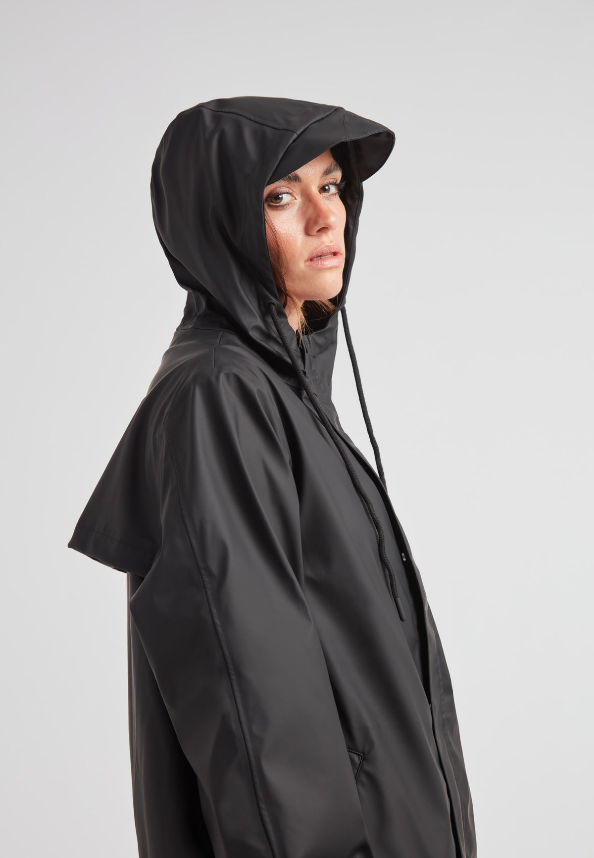 Woman wearing the ELEMENTS Raincoat 2.0 Black, featuring a hood and sleek black design for versatile weather protection.