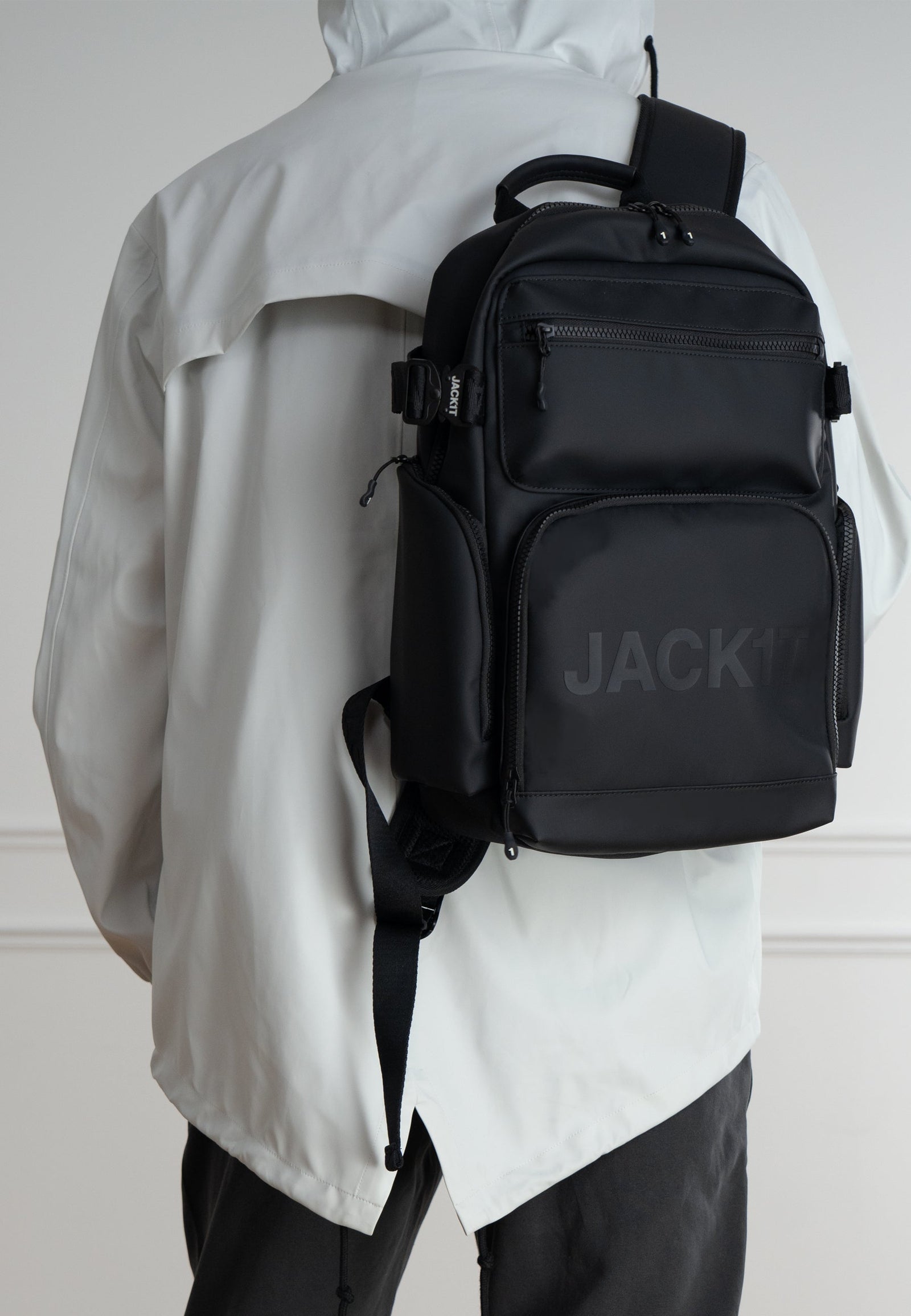 Person wearing JACK1T's black water resistant backpack while dressed in a stylish, light jacket.