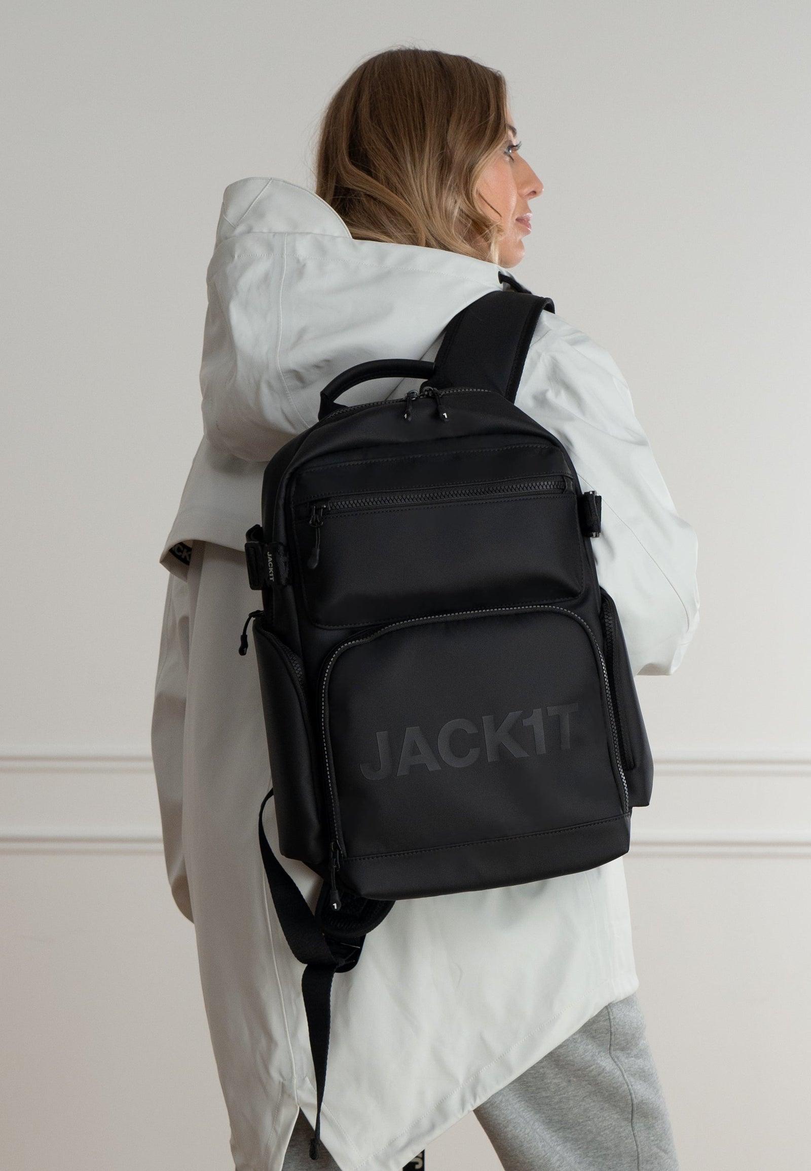 JACK1T's black water resistant backpack worn by a woman in a stylish outfit, showcasing modern design and functionality.