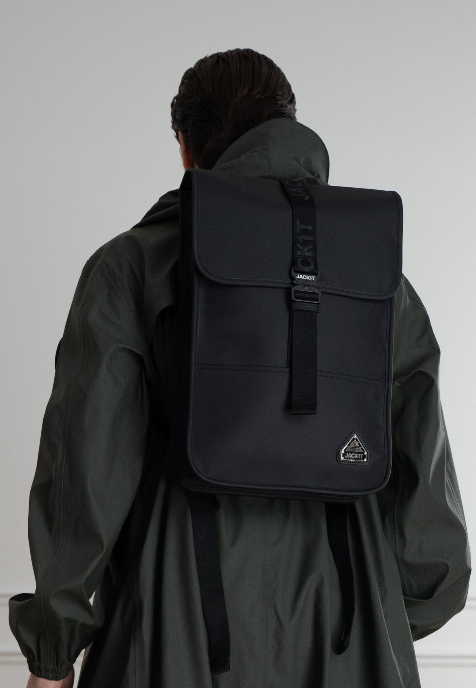 The JACK1T slim messenger laptop bag in black worn on the back of a person with a green coat.