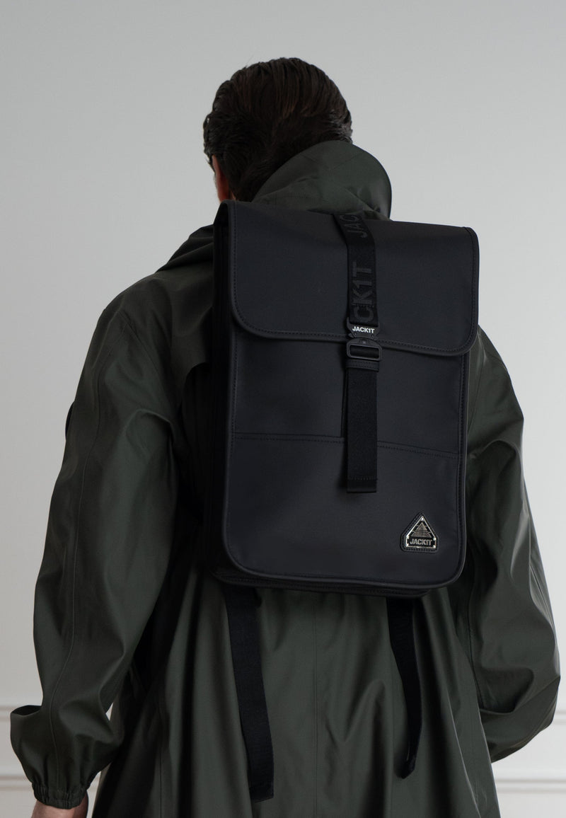 The JACK1T slim messenger laptop bag in black worn on the back of a person with a green coat.