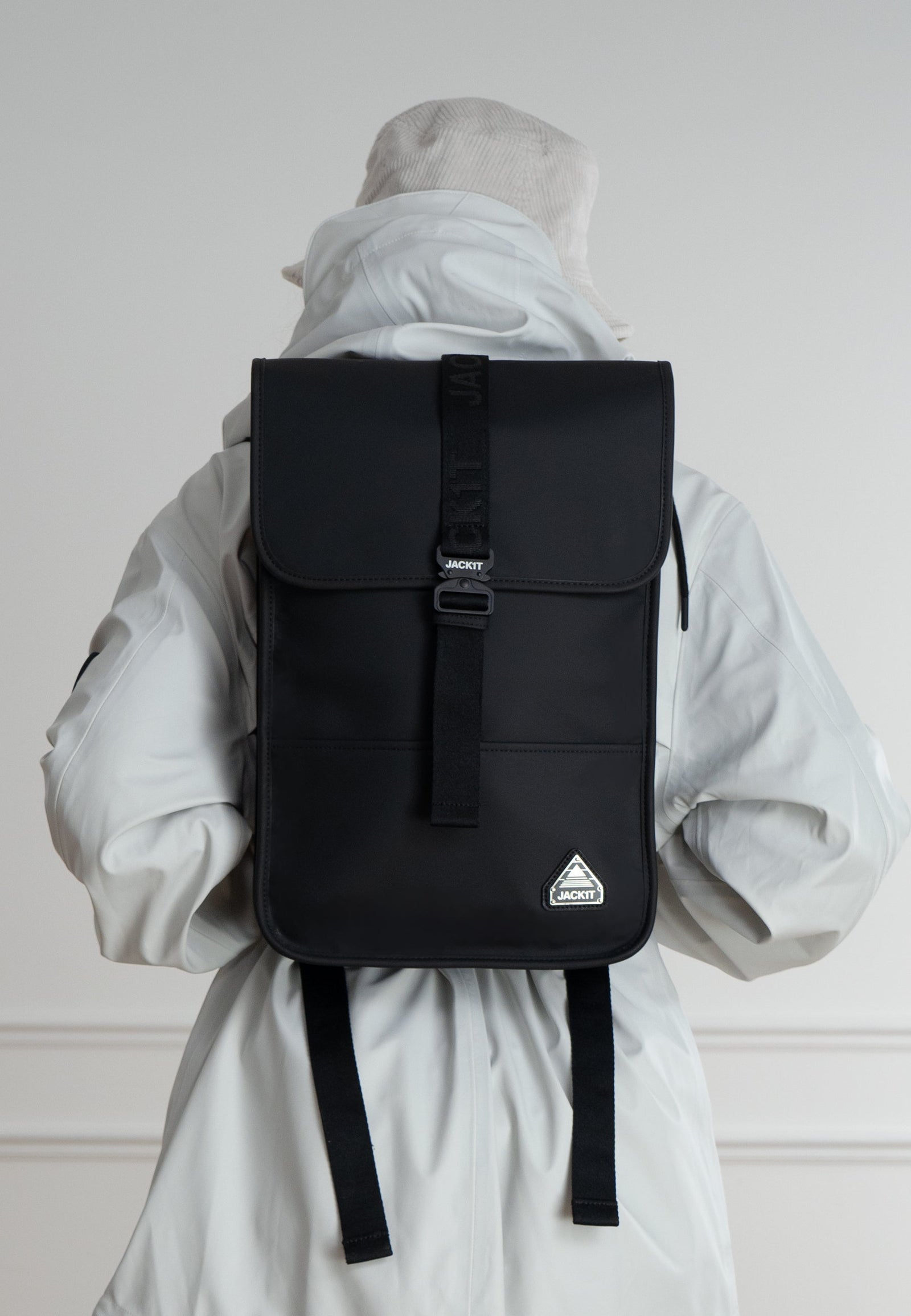 The JACK1T slim messenger laptop bag in black worn by a person in a white jacket from behind.