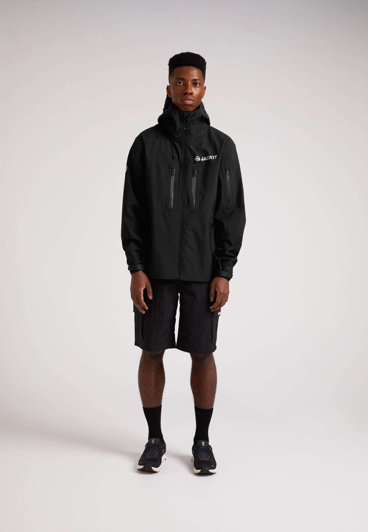 Black mens Lithium waterproof jacket worn by a model standing in shorts and sneakers against a plain background.