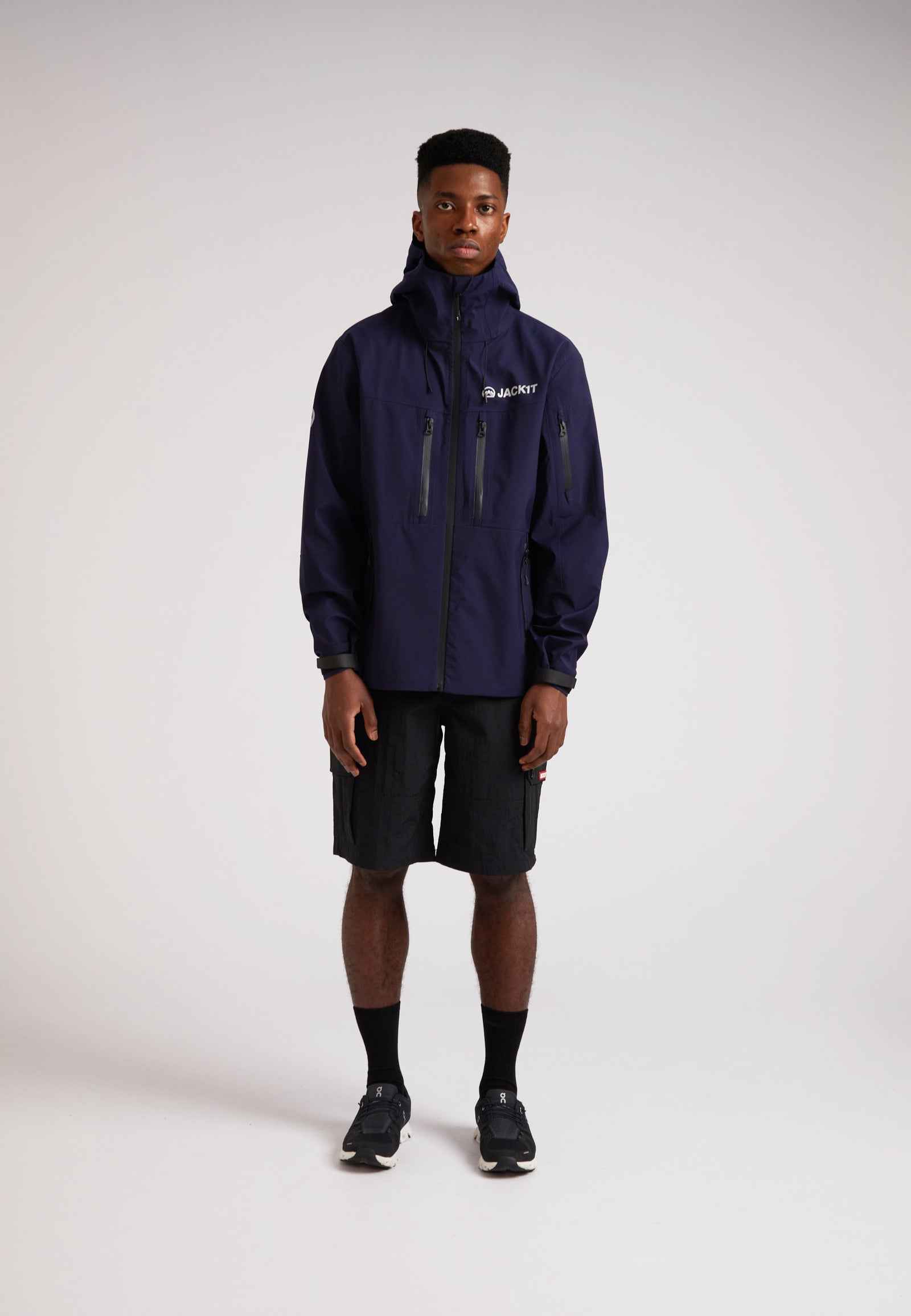Model wearing a navy lithium waterproof mens jacket with shorts, showcasing its sleek design and functionality.