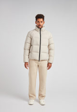 Man wearing the Cloud Lightweight Puffer Racer Jacket Stone with light beige puffer jacket and cream pants.