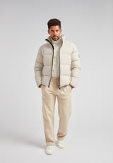 Model wearing Cloud Lightweight Puffer Racer Jacket Stone with casual pants on gray background.