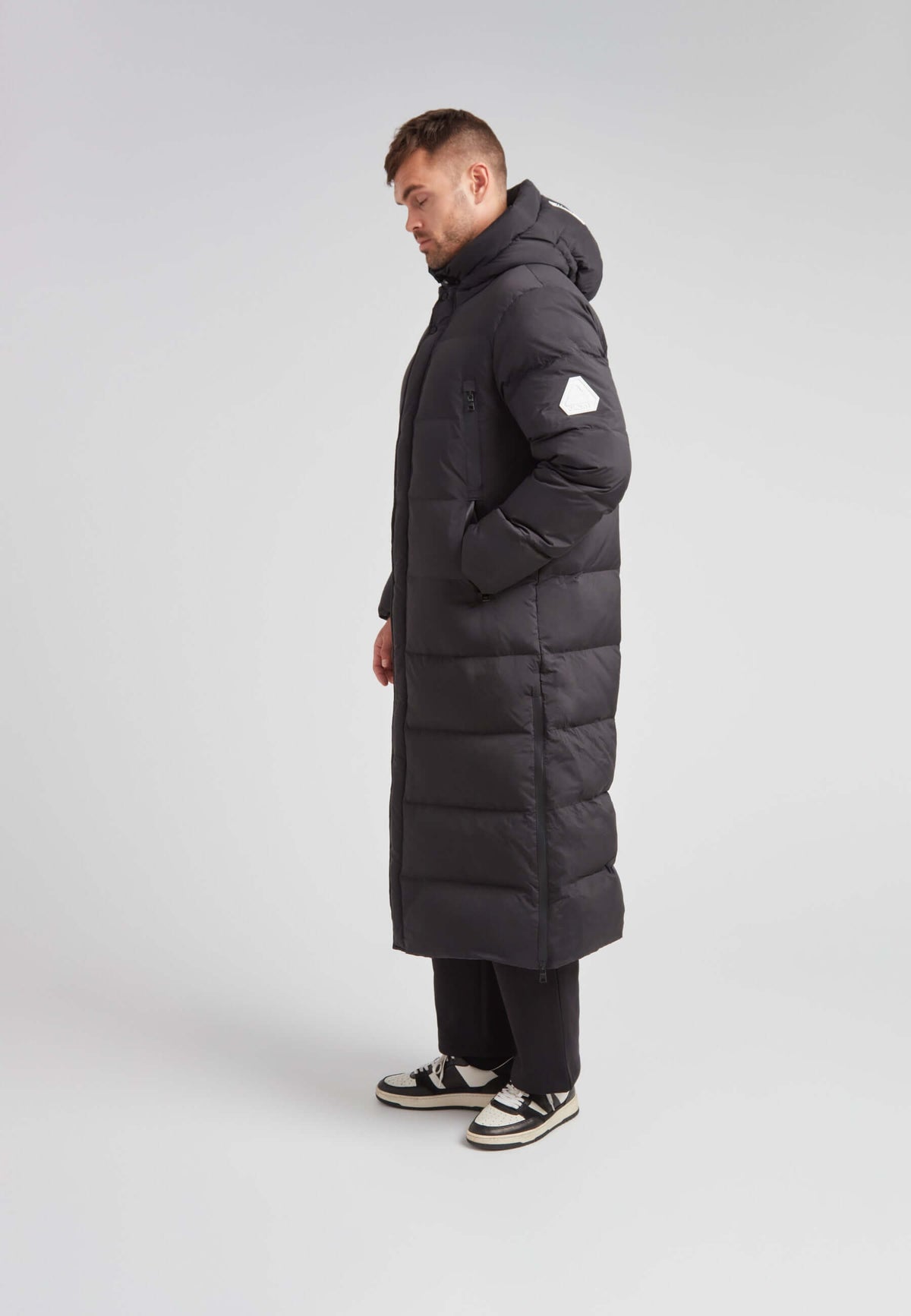 Mens Extra Long Puffer Coat in Black shown side view, highlighting its ankle-length and stylish silhouette.