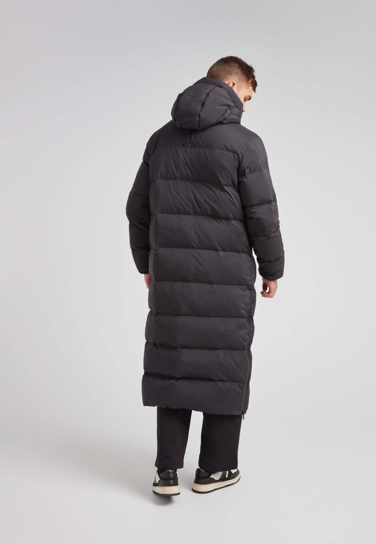 Mens Extra Long Puffer Coat in Black worn from the back, featuring a hood and puffy quilted design.