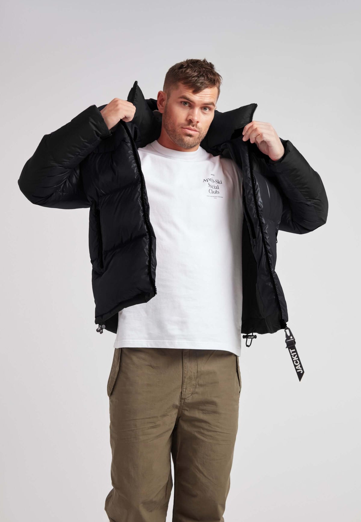 Man wearing Expedition Parka Puffer Men Black jacket, preparing to zip it up.