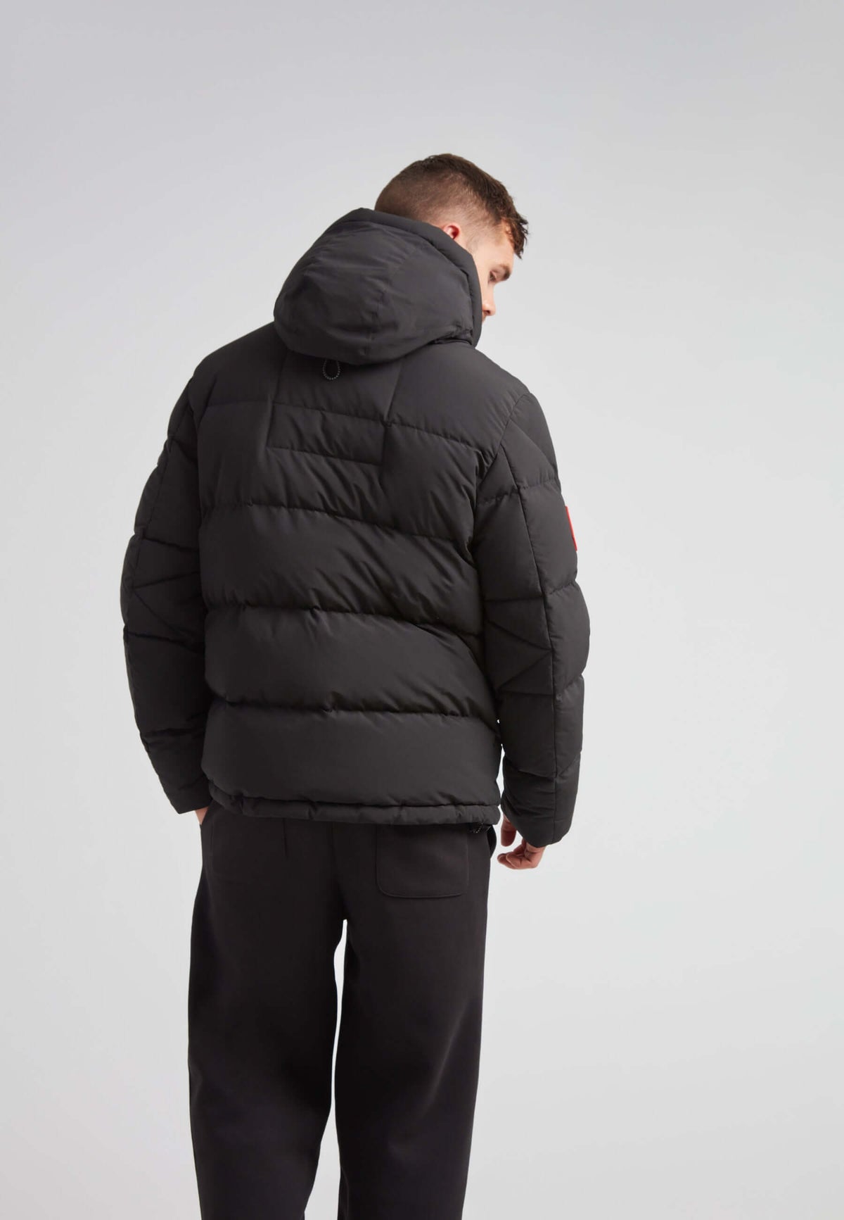 Back view of a model wearing the EZ Frontier Prime Down Puffer Jacket Matt Black, featuring a hood and puffer design.
