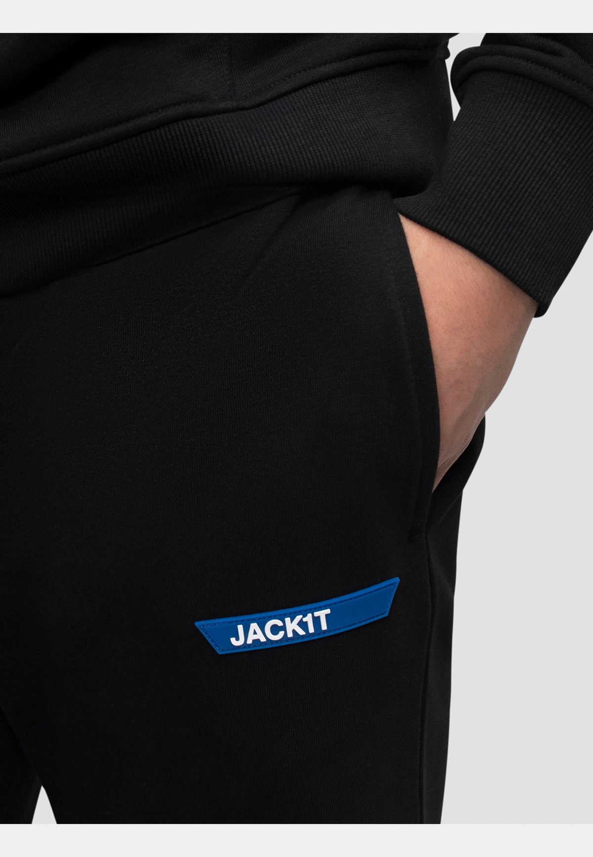 Close-up of black joggers featuring a blue JACKIT logo and side pocket for a stylish and comfortable look.