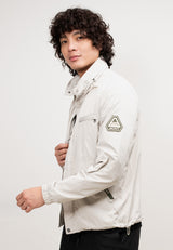 Model wearing the Atlas Lightweight Windbreaker Stone, showcasing a stylish, windproof design and roll-out hood.