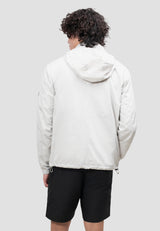 Back view of a male model wearing the Atlas Lightweight Windbreaker Stone, featuring a roll-out hood and elasticated cuffs.