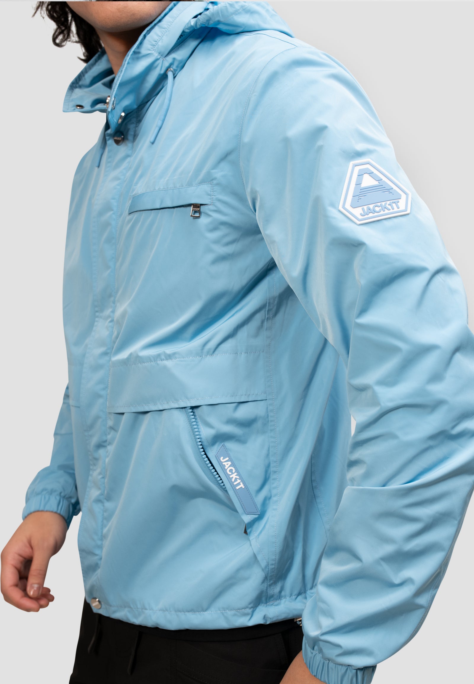Mens lightweight sky blue windbreaker displayed on model, showcasing roll out hood and front pocket.