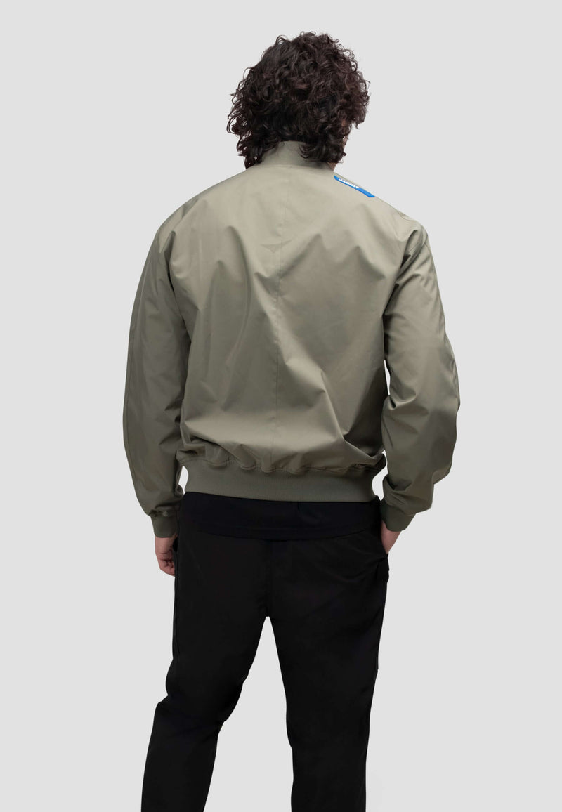 Back view of a model wearing a mens olive bomber jacket in dusty olive color.