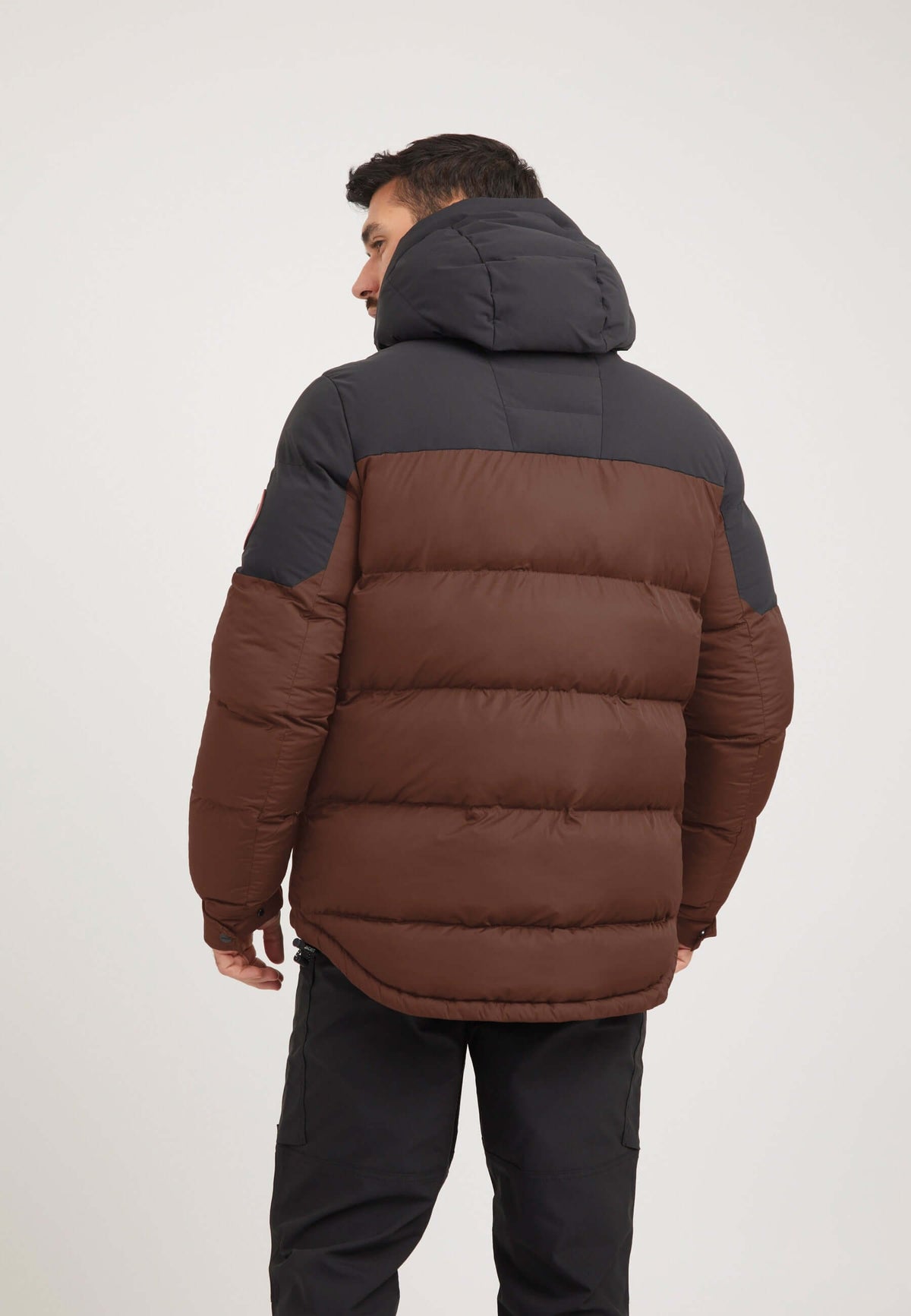 Back view of a man wearing a mens brown puffer jacket in mid brown and black color combination.