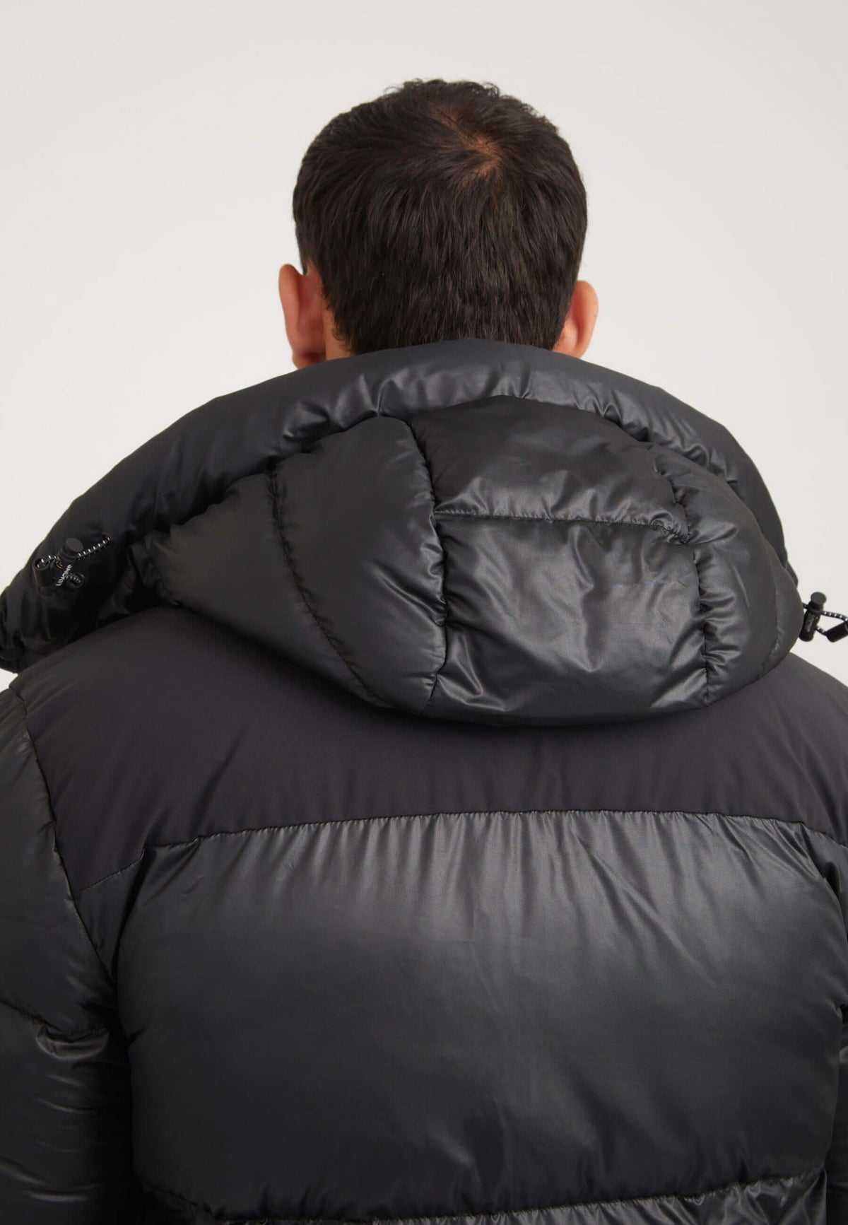 Man wearing a Mens black parka with an oversized removable hood and boxy fit silhouette.
