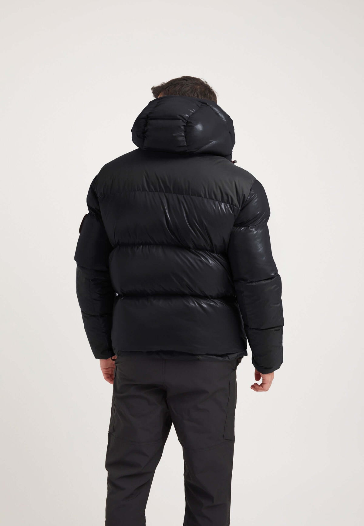 Back view of a man wearing a mens black parka with an oversized hood and puffy design.