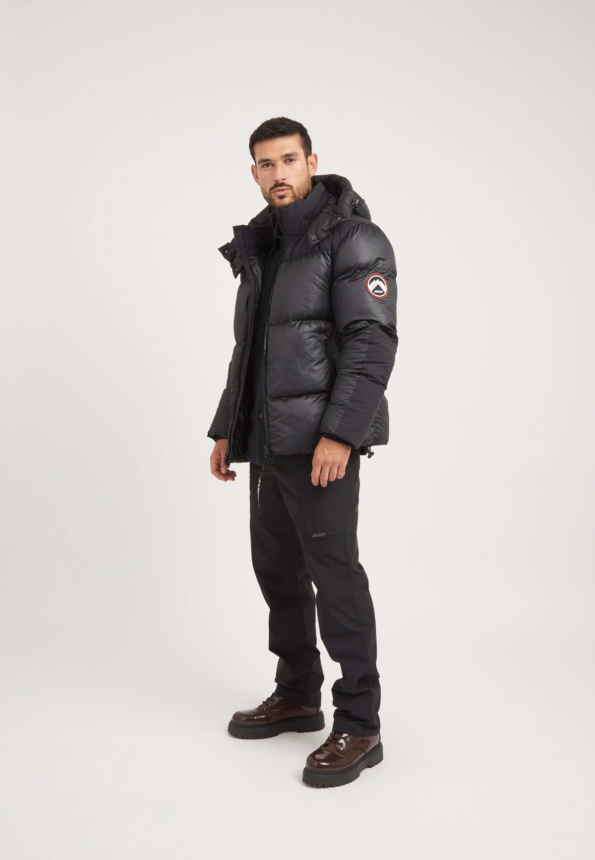 Model wearing a mens black parka with oversized hood and contrasting colour panels, featuring premium insulation.