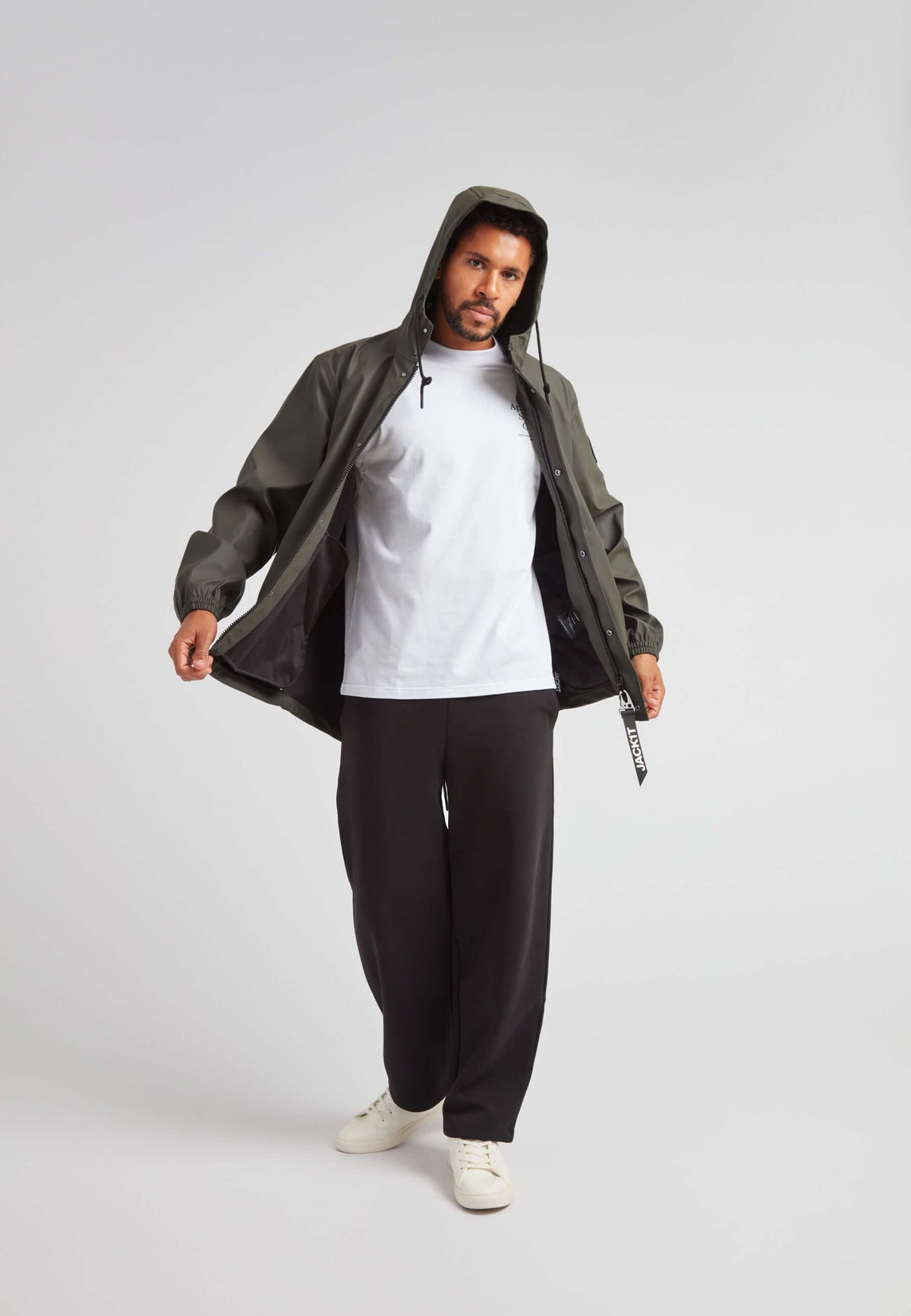 Man wearing ELEMENTS Unisex Raincoat 2.0 Khaki with a hood, styled with a white t-shirt and black pants.