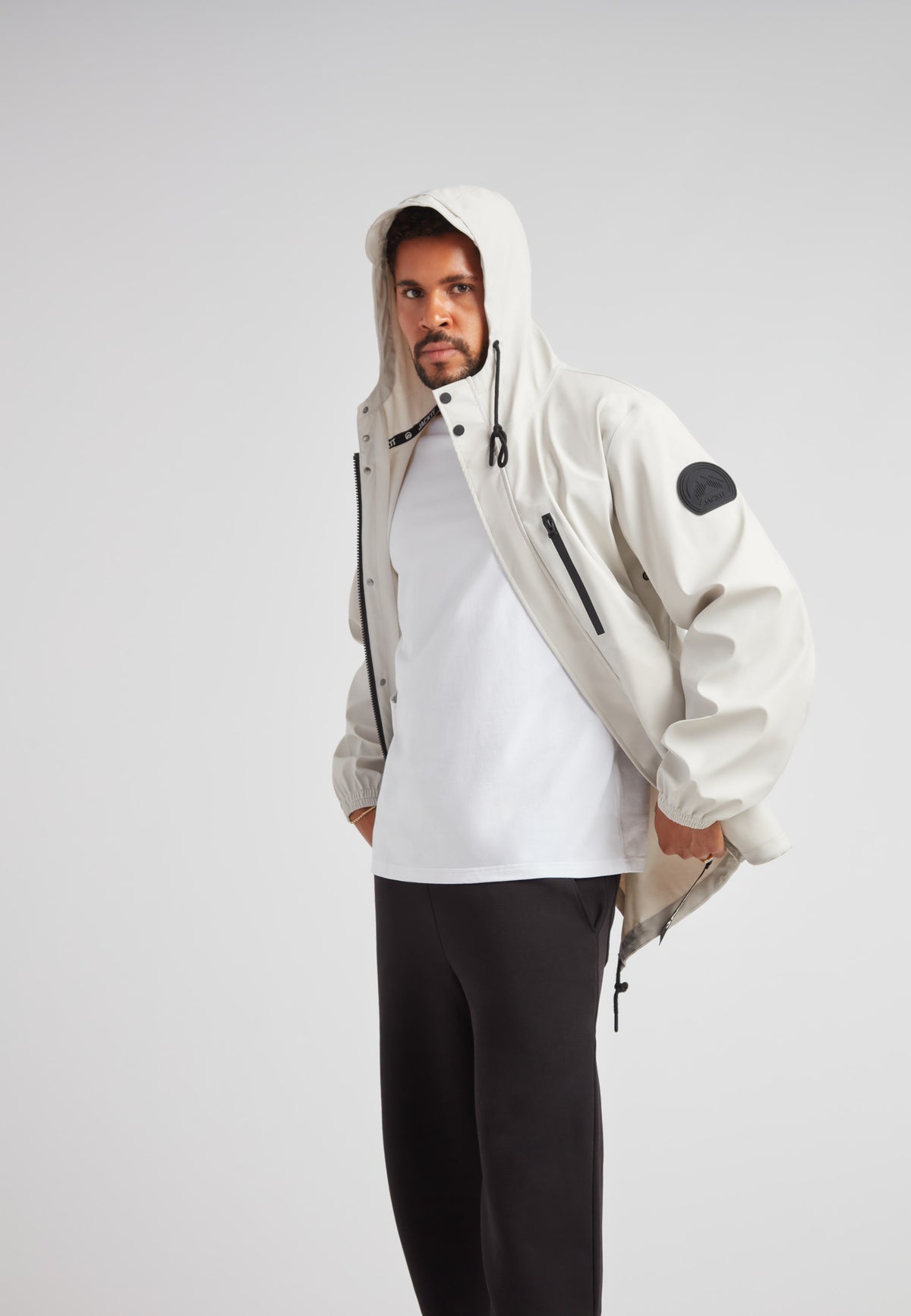 Model wearing ELEMENTS Unisex Raincoat 2.0 Stone with hood in stylish casual outfit.
