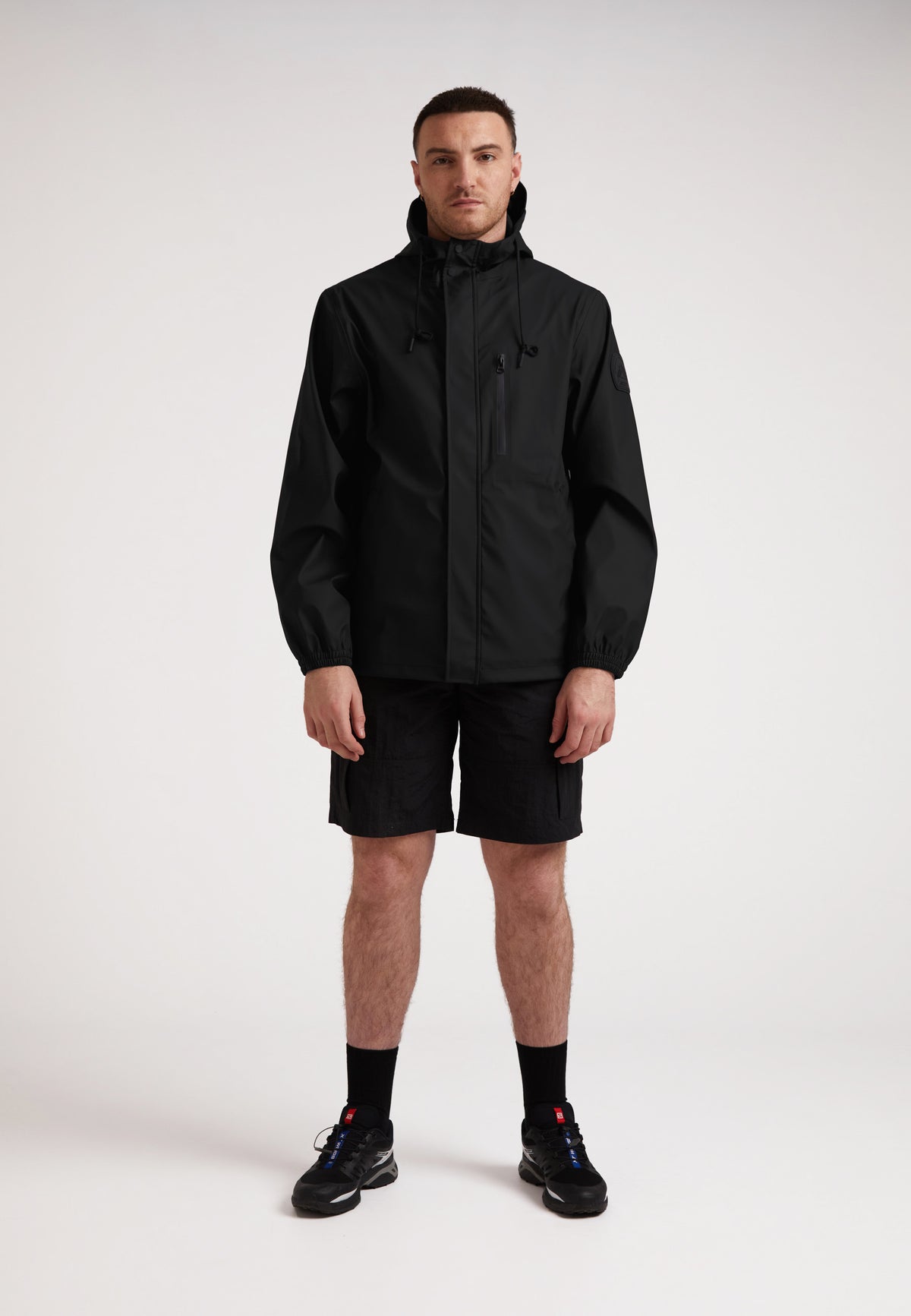Model wearing ELEMENTS Unisex Raincoat 2.0 Black with shorts and sneakers.