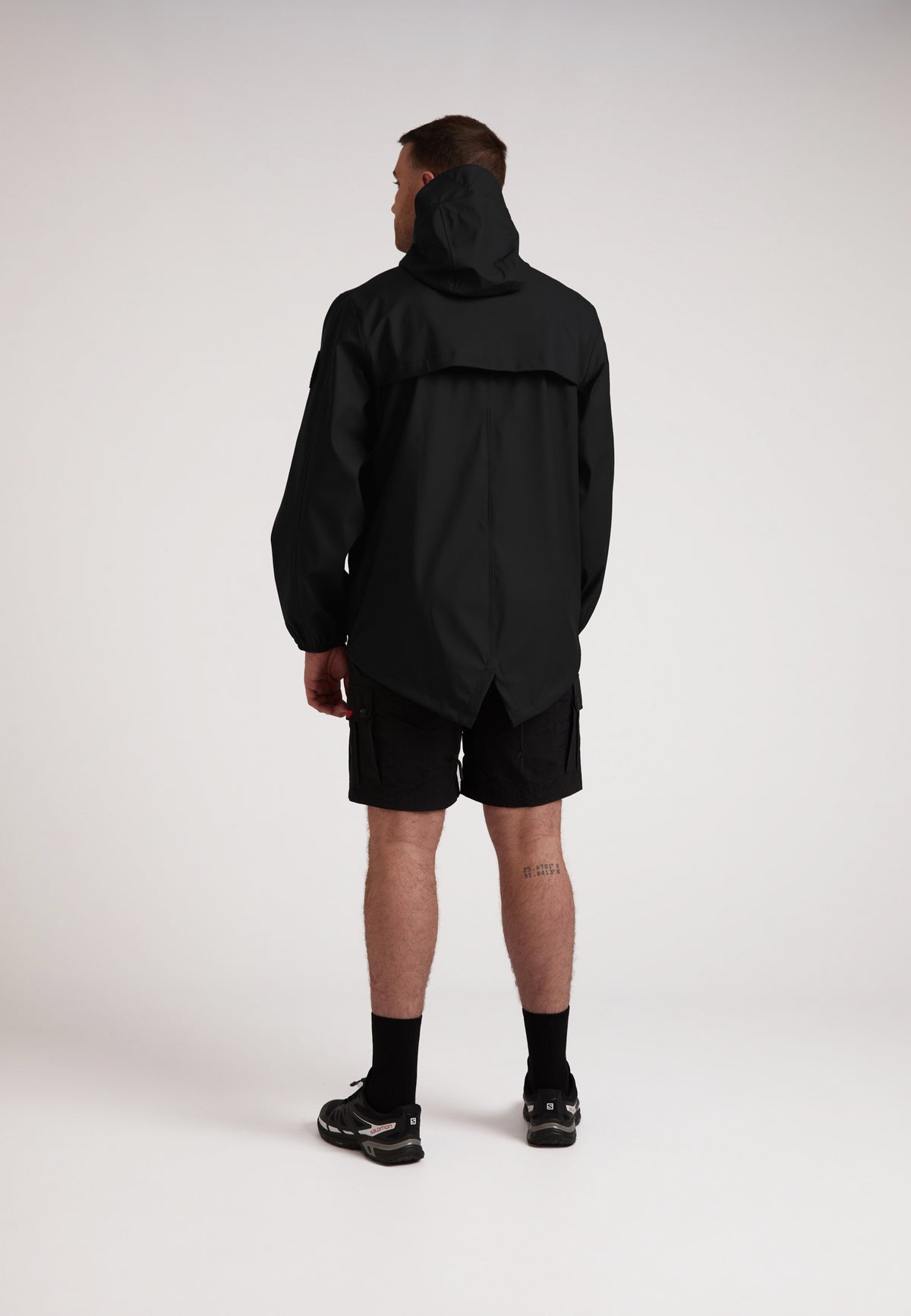 Back view of a model wearing the ELEMENTS Unisex Raincoat 2.0 Black with shorts, showcasing its lightweight design.
