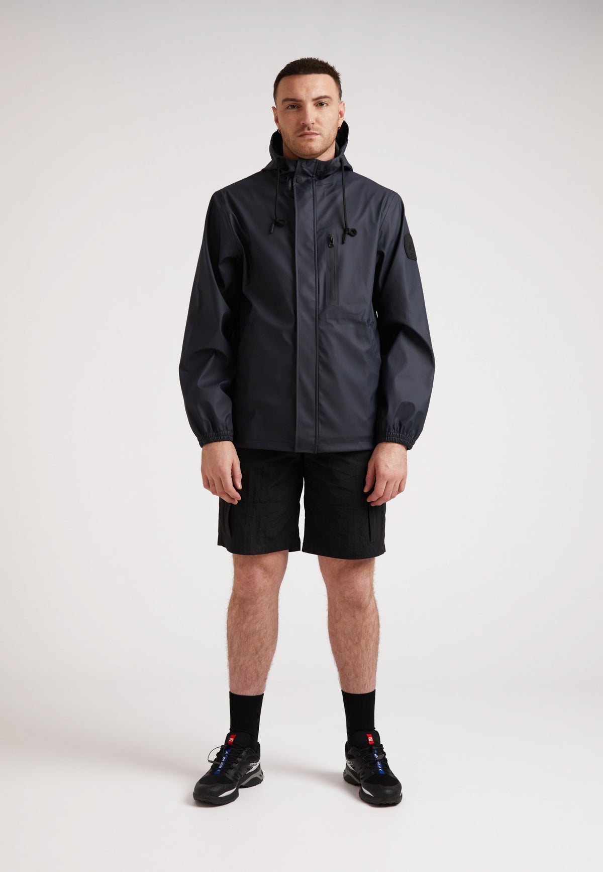 A model wearing the ELEMENTS Unisex Raincoat 2.0 Navy with shorts, showcasing versatile weather protection.