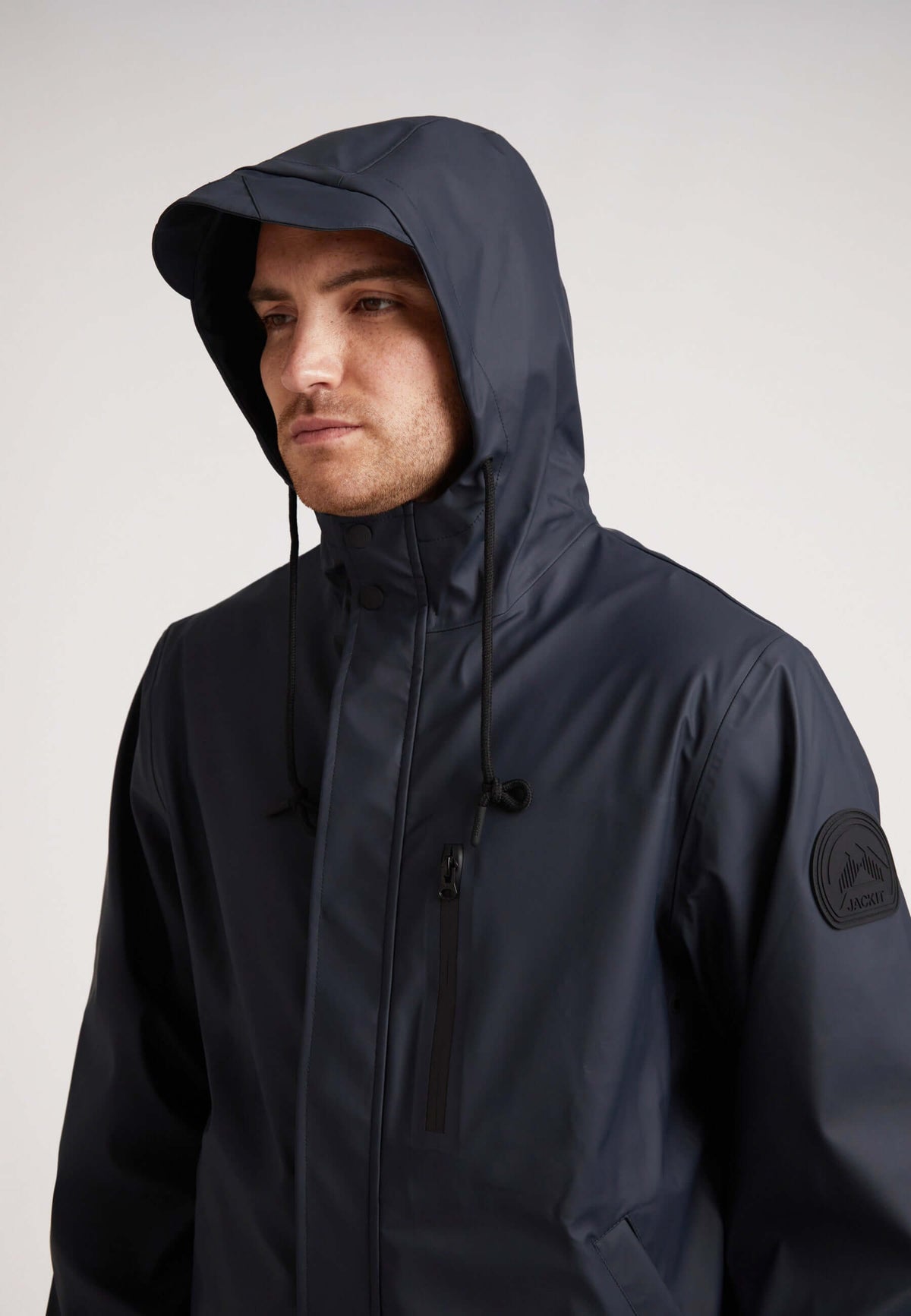 Man wearing ELEMENTS Unisex Raincoat 2.0 Navy with hood up, showcasing lightweight weather protection.
