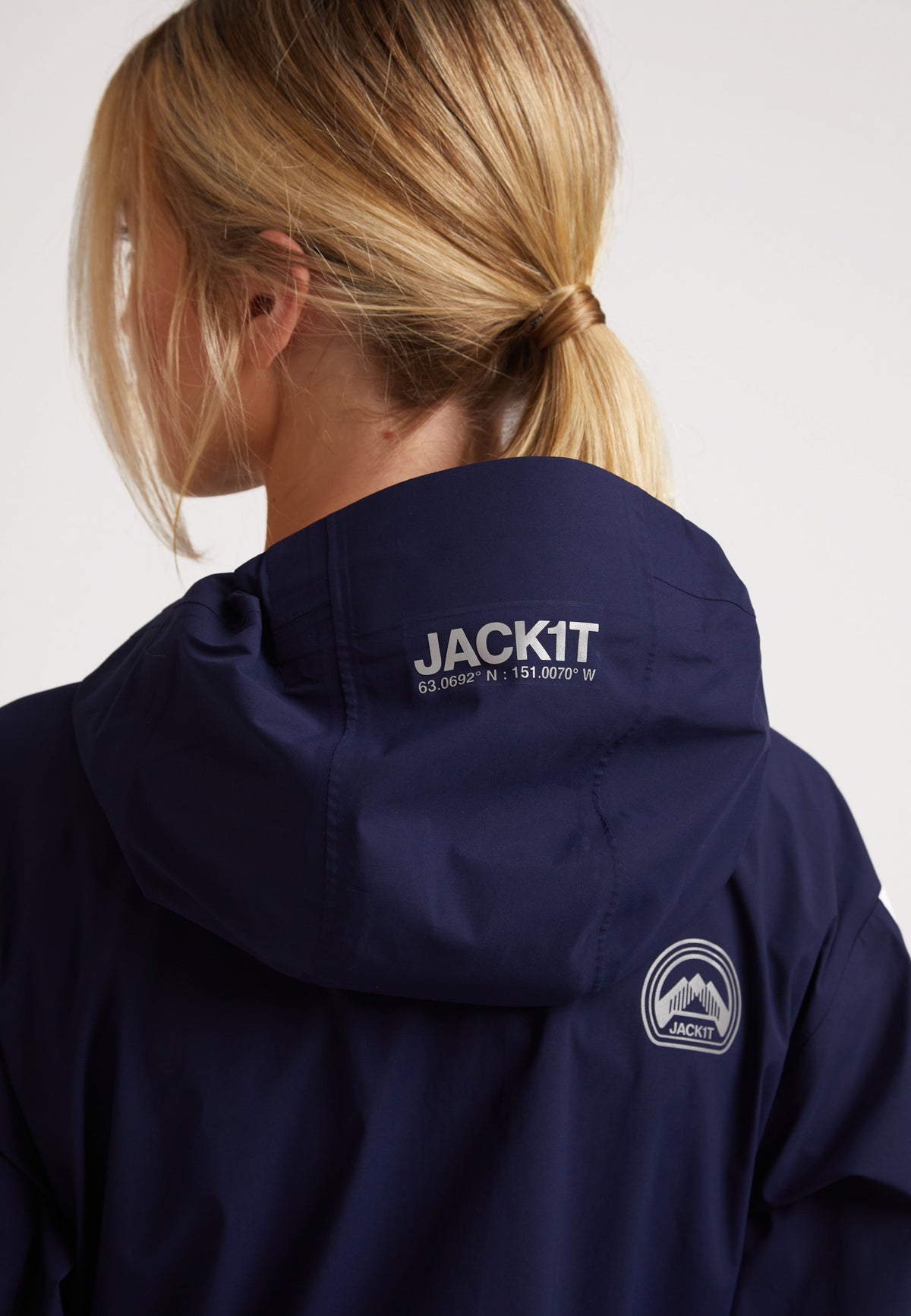 Back view of a woman wearing a navy jacket with hood, featuring logo and waterproof design, highlighting its stylish and functional features.