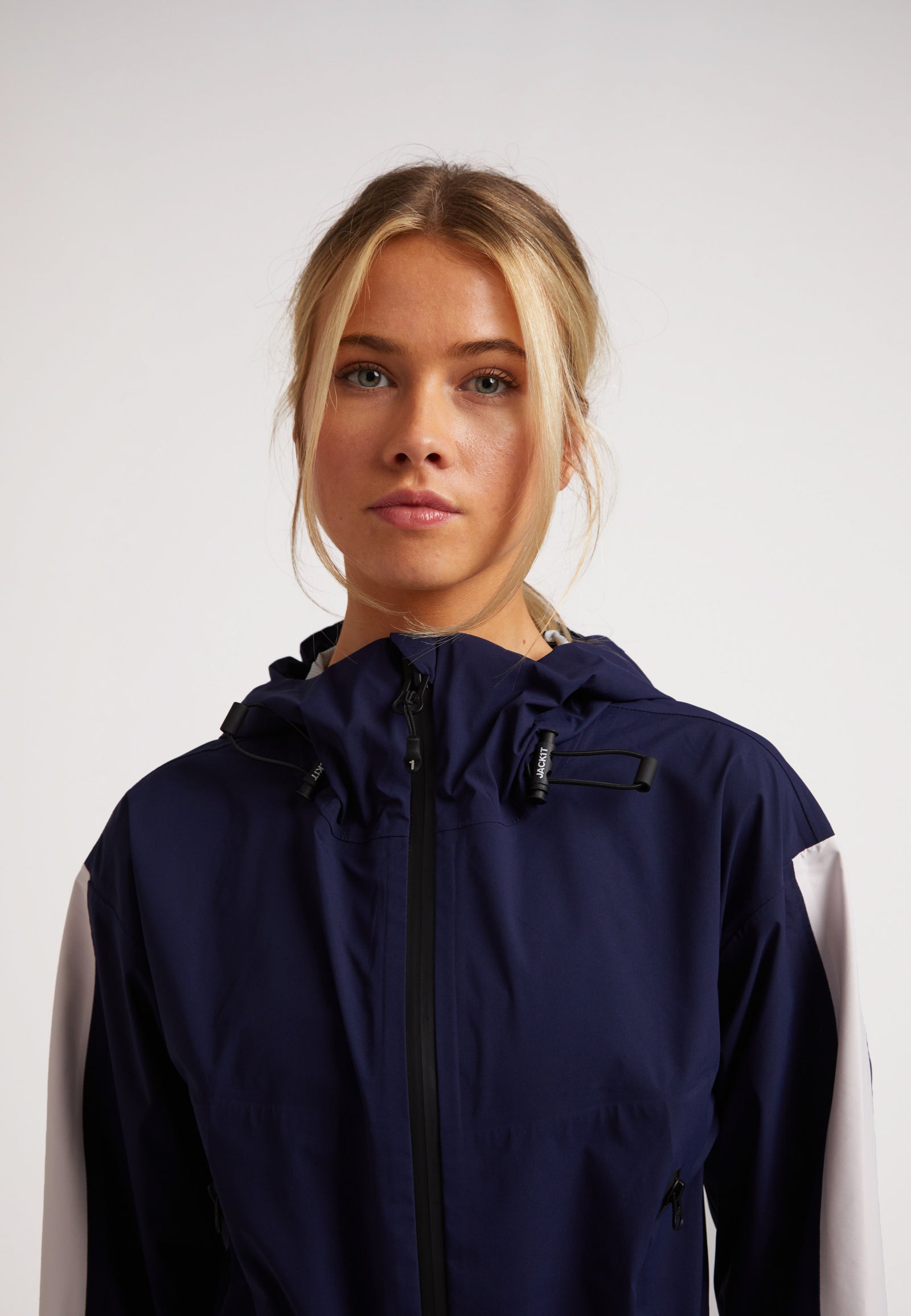 Model wearing a Ladies waterproof lightweight navy jacket with adjustable hood and zippers.