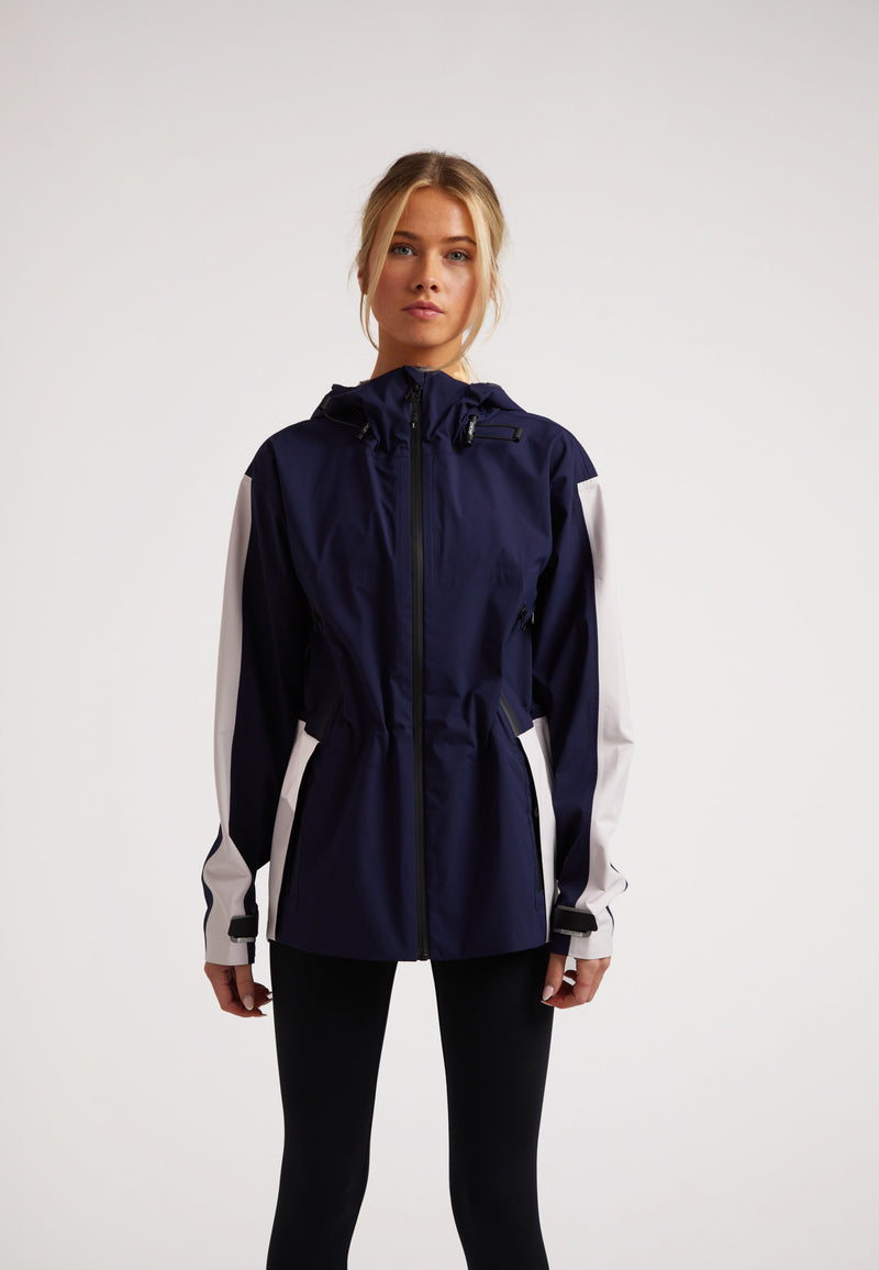 Model wearing a Ladies waterproof lightweight navy jacket with adjustable hood and cuffs, designed for performance in various weather.