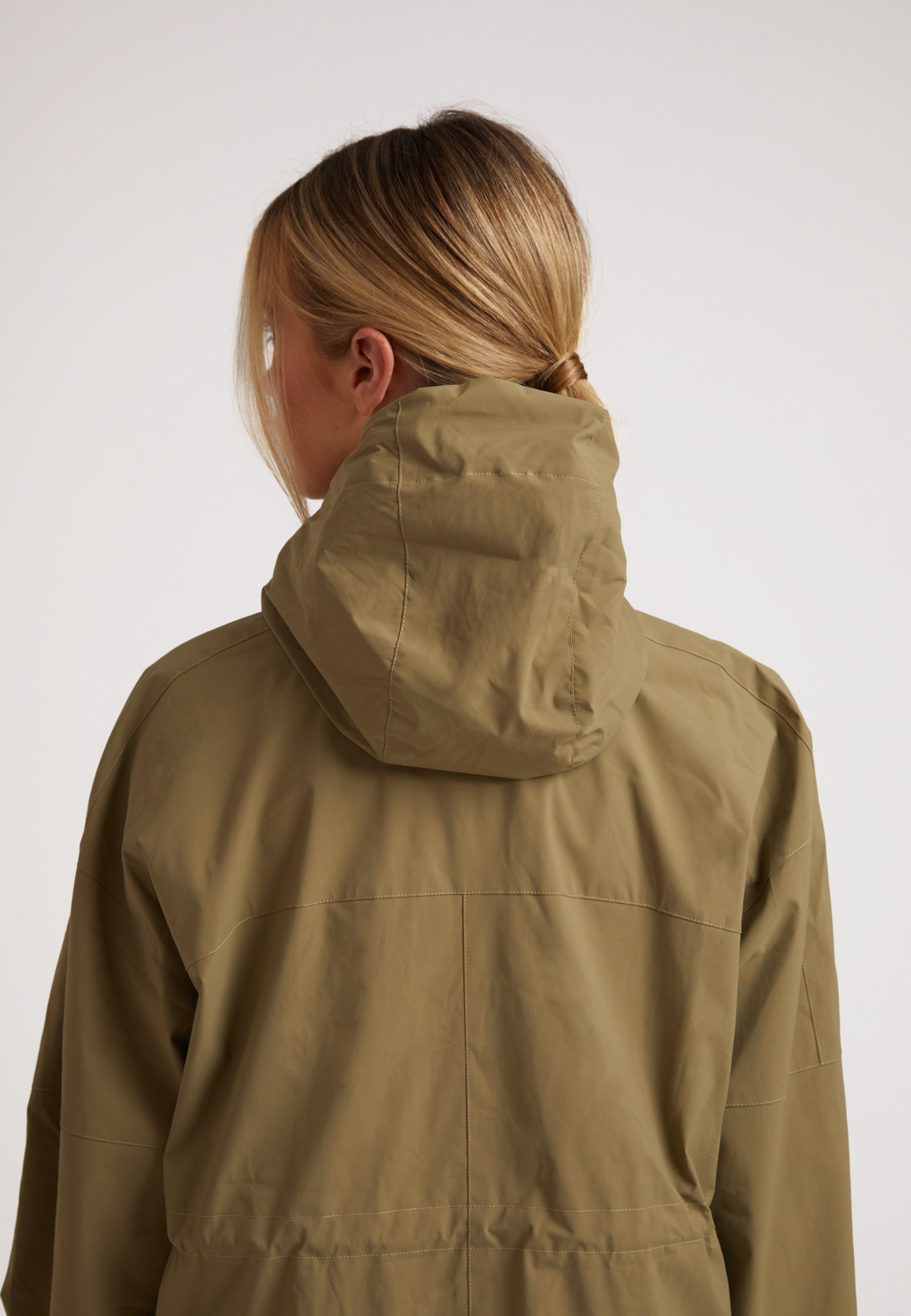 Back view of model wearing ISOTOPE lightweight windbreaker, showcasing hood and olive color. Ladies lightweight olive windbreaker.