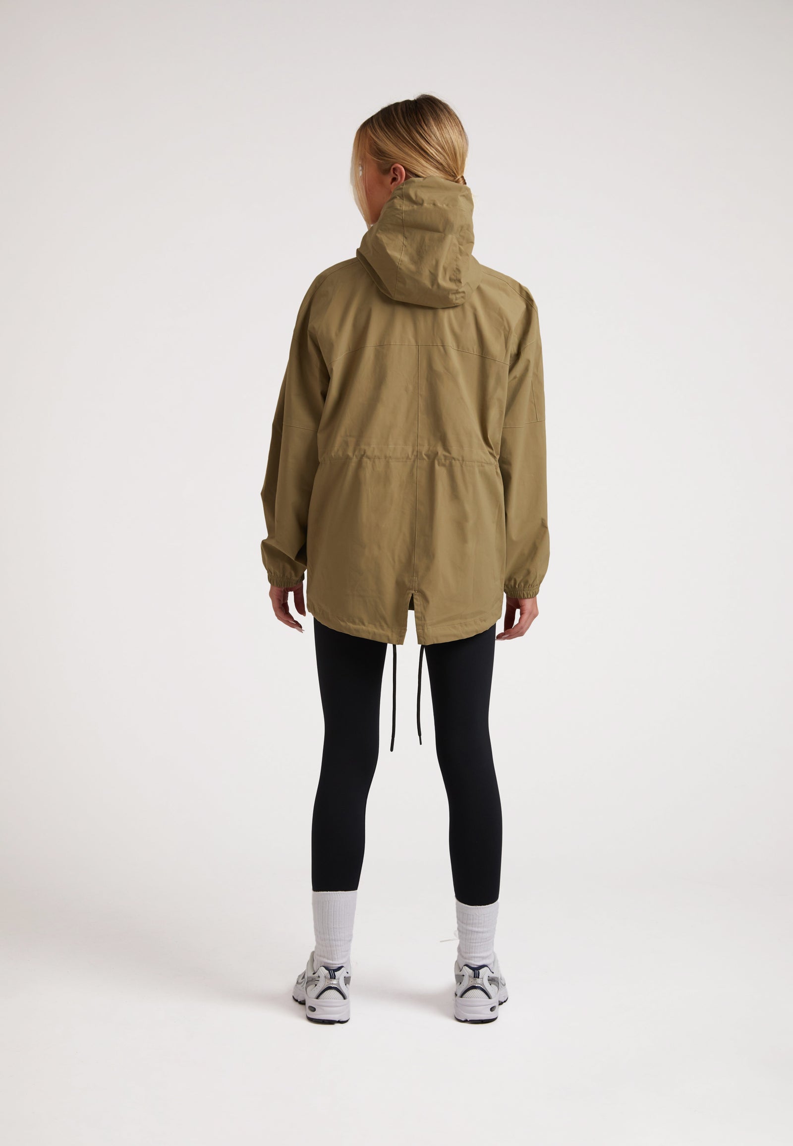 Back view of a model wearing a Ladies lightweight olive windbreaker with adjustable hem and hood.