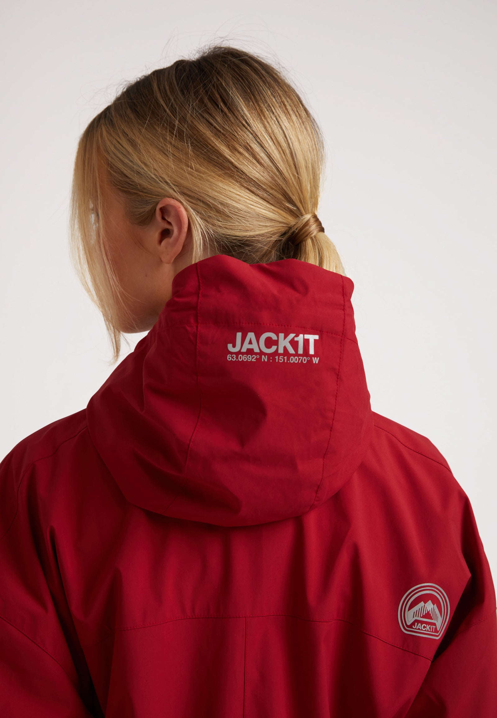 A woman wearing a ladies red lightweight windbreaker, with a focus on the jacket's hood and back design.