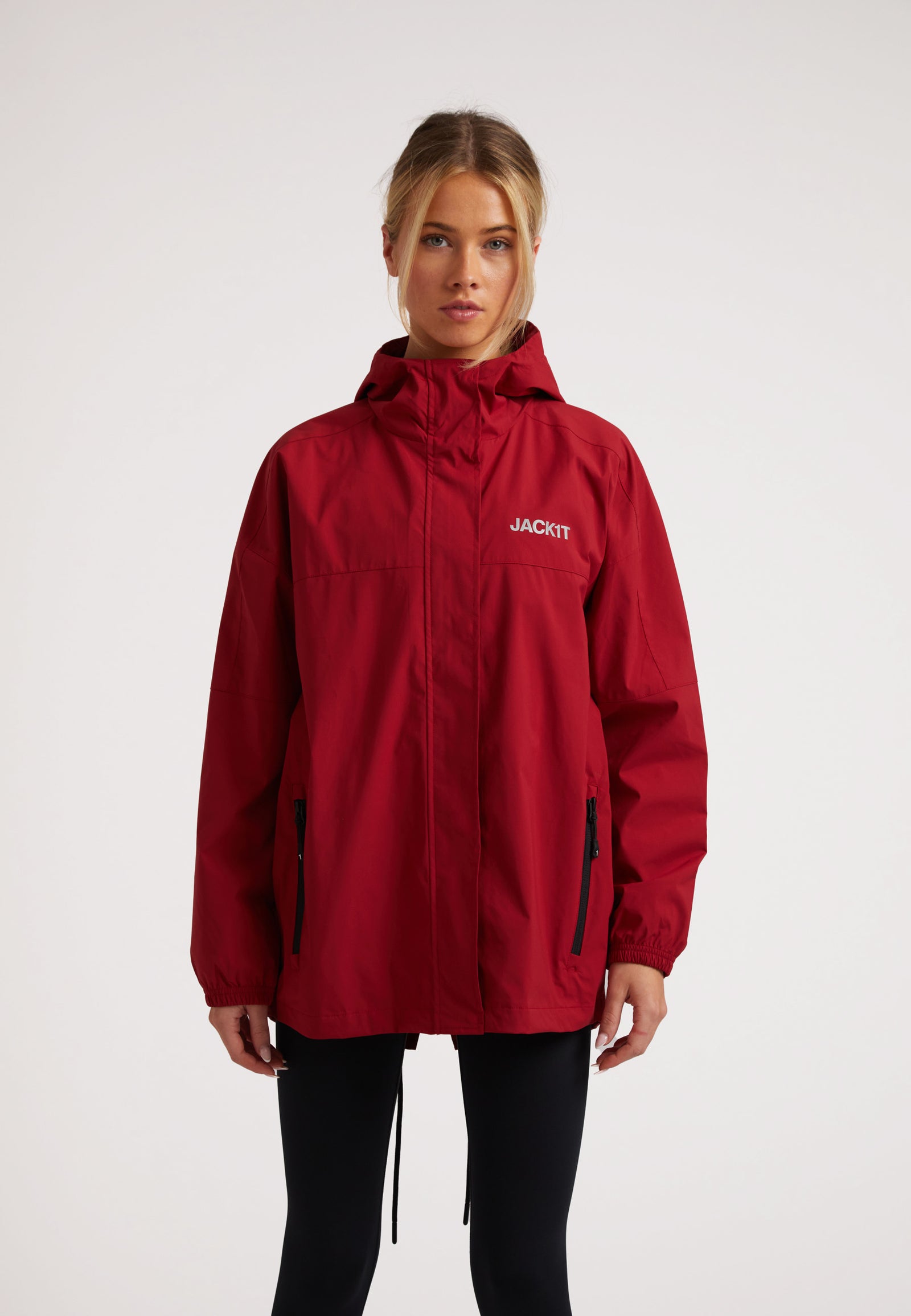 Ladies red lightweight windbreaker model wearing a red jacket with a hood, featuring zippers and a relaxed fit.