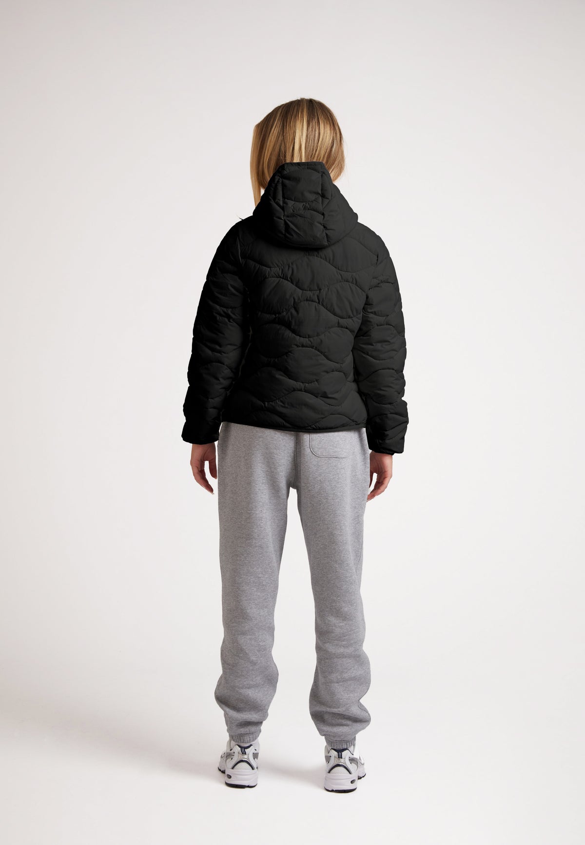 Back view of a model wearing the ORB1T Quilted Puffer Jacket styled with gray sweatpants.