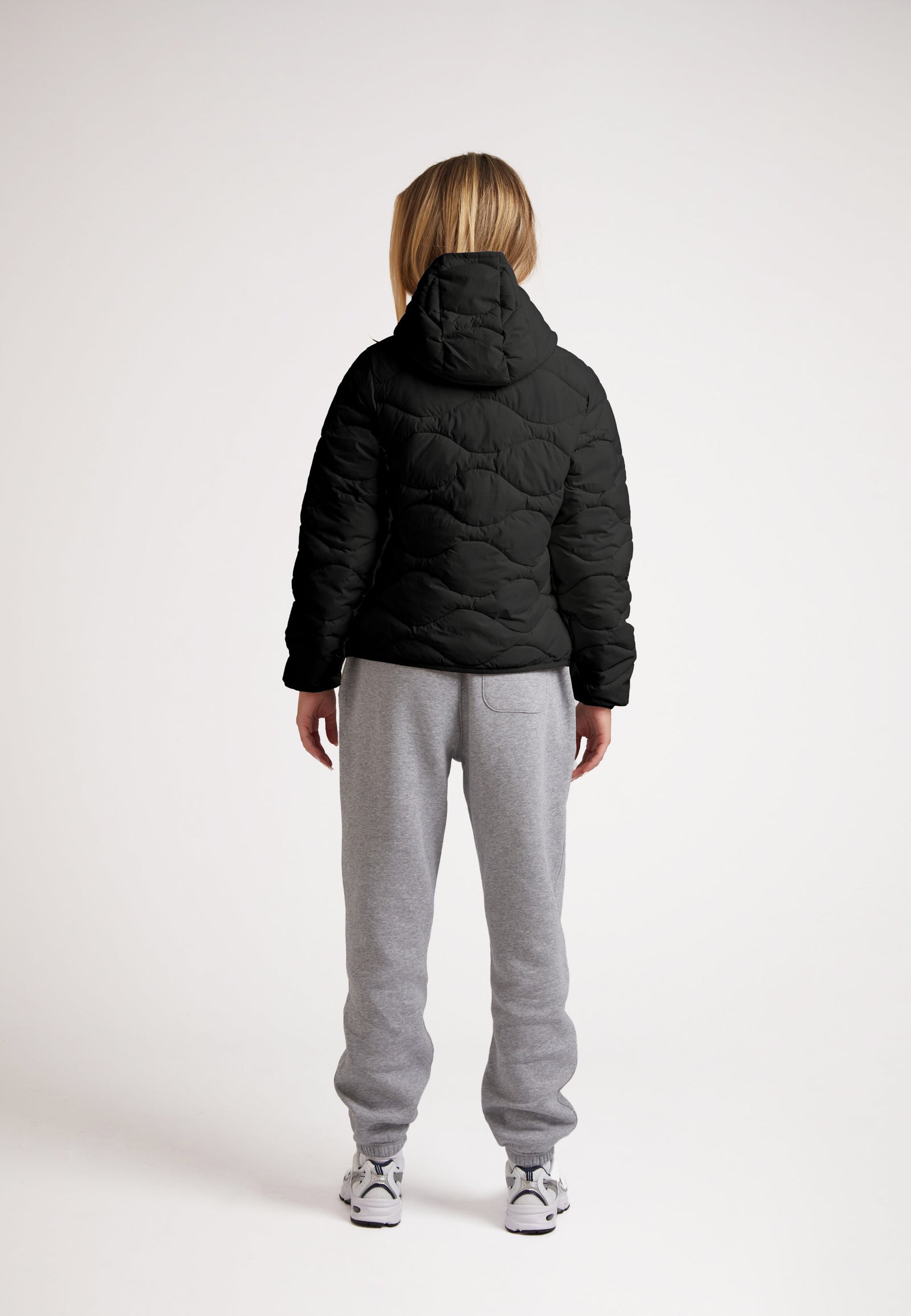 Back view of a model wearing the ORB1T Quilted Puffer Jacket styled with gray sweatpants.