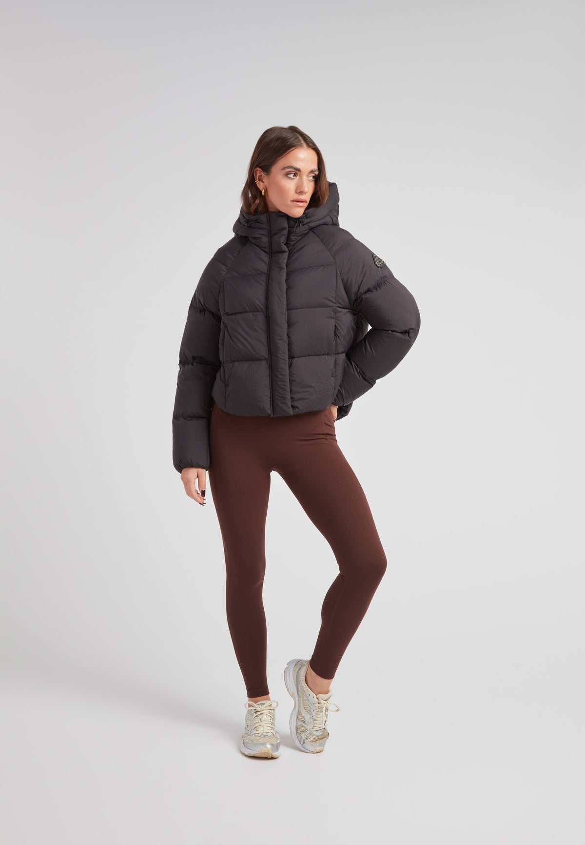 Model wearing the Cloud Crop Down Puffer Jacket Black with brown leggings and sneakers in a setting.