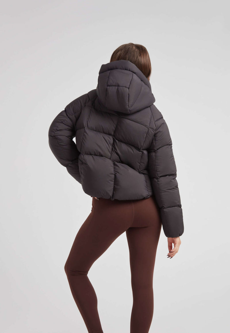 Back view of a woman wearing a short puffer jacket women, showcasing its oversized hood and cropped design.