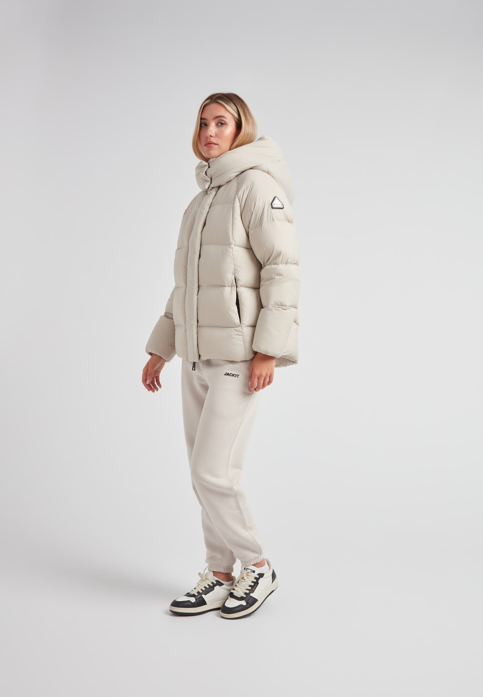 Woman wearing the Cloud Prime Longline Down Puffer Jacket Stone, styled with casual sweatpants and sneakers.