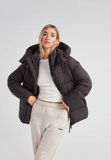 Woman wearing the Cloud Prime Longline Down Puffer Jacket in black, styled with a white top and beige pants.
