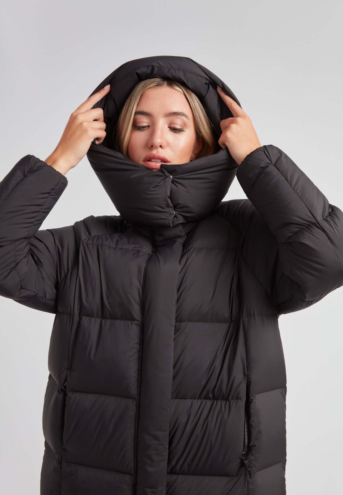Woman adjusting hood on Cloud Ultra Long Down Puffer Coat, the ideal long puffer jacket in black for winter warmth.