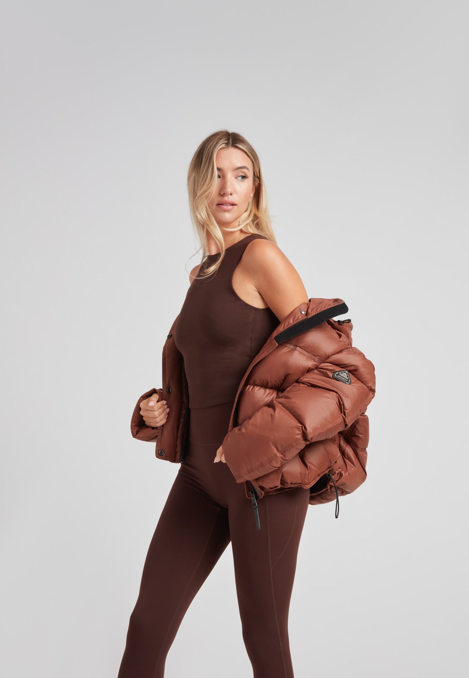 Model wearing a cropped puffer in mocha brown with adjustable coverage, featuring oversized design and stylish streetwear appeal.