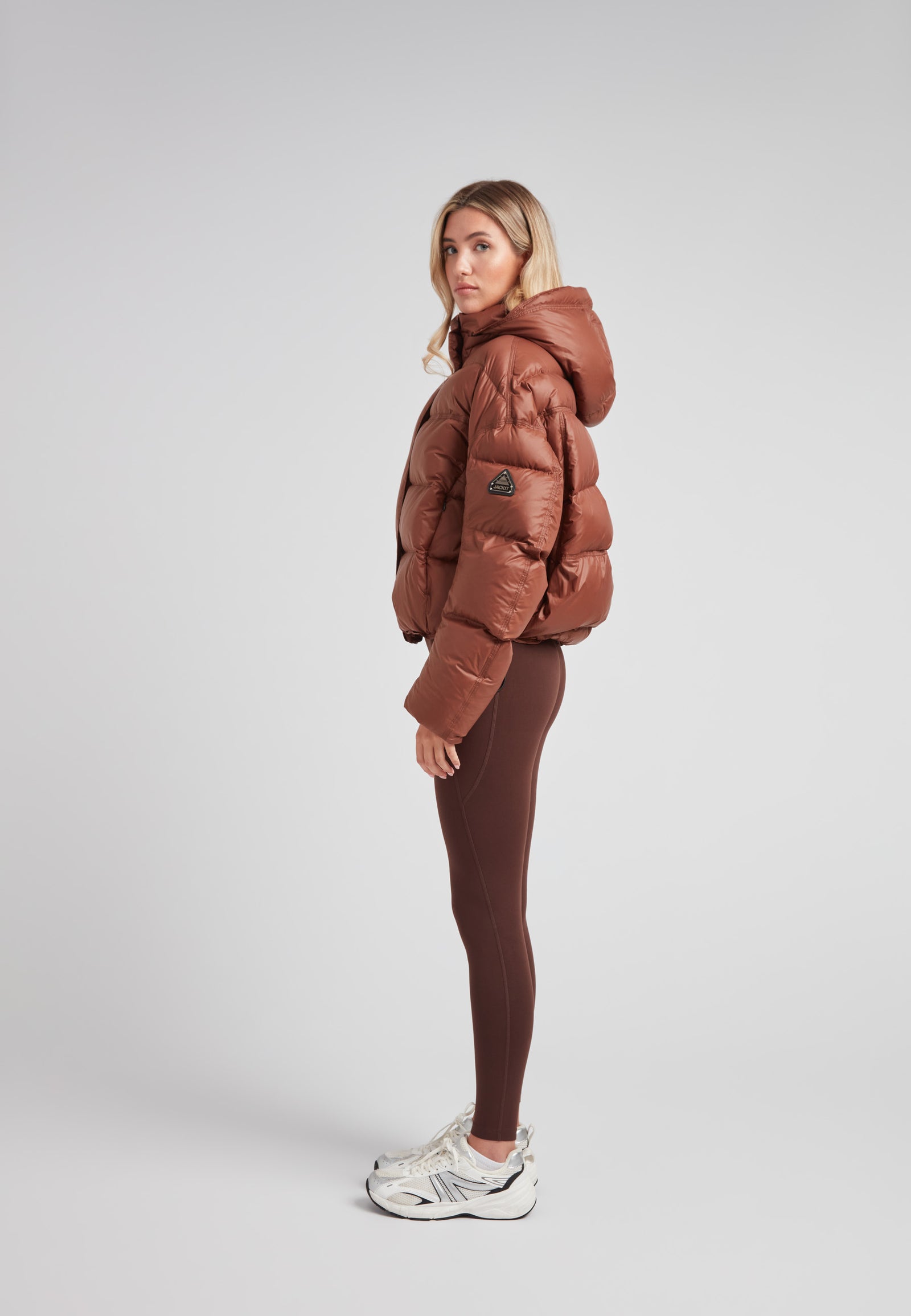 Cropped puffer in mocha brown with adjustable coverage worn by a model, showcasing street style and warmth.