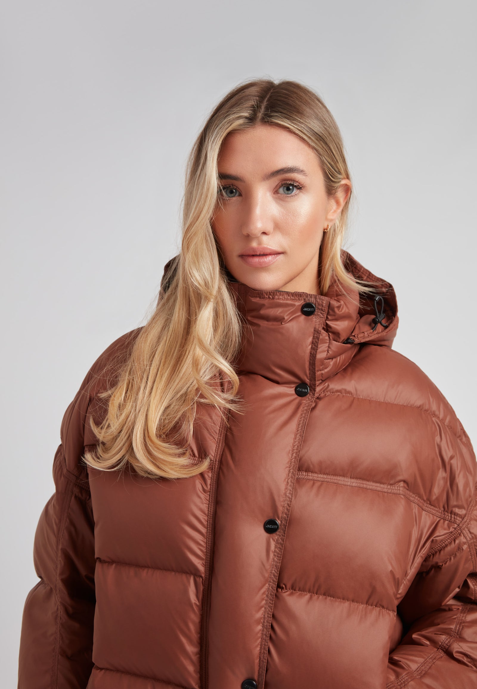 Cropped puffer in mocha brown with adjustable coverage, showcasing a model wearing a stylish oversized down jacket.